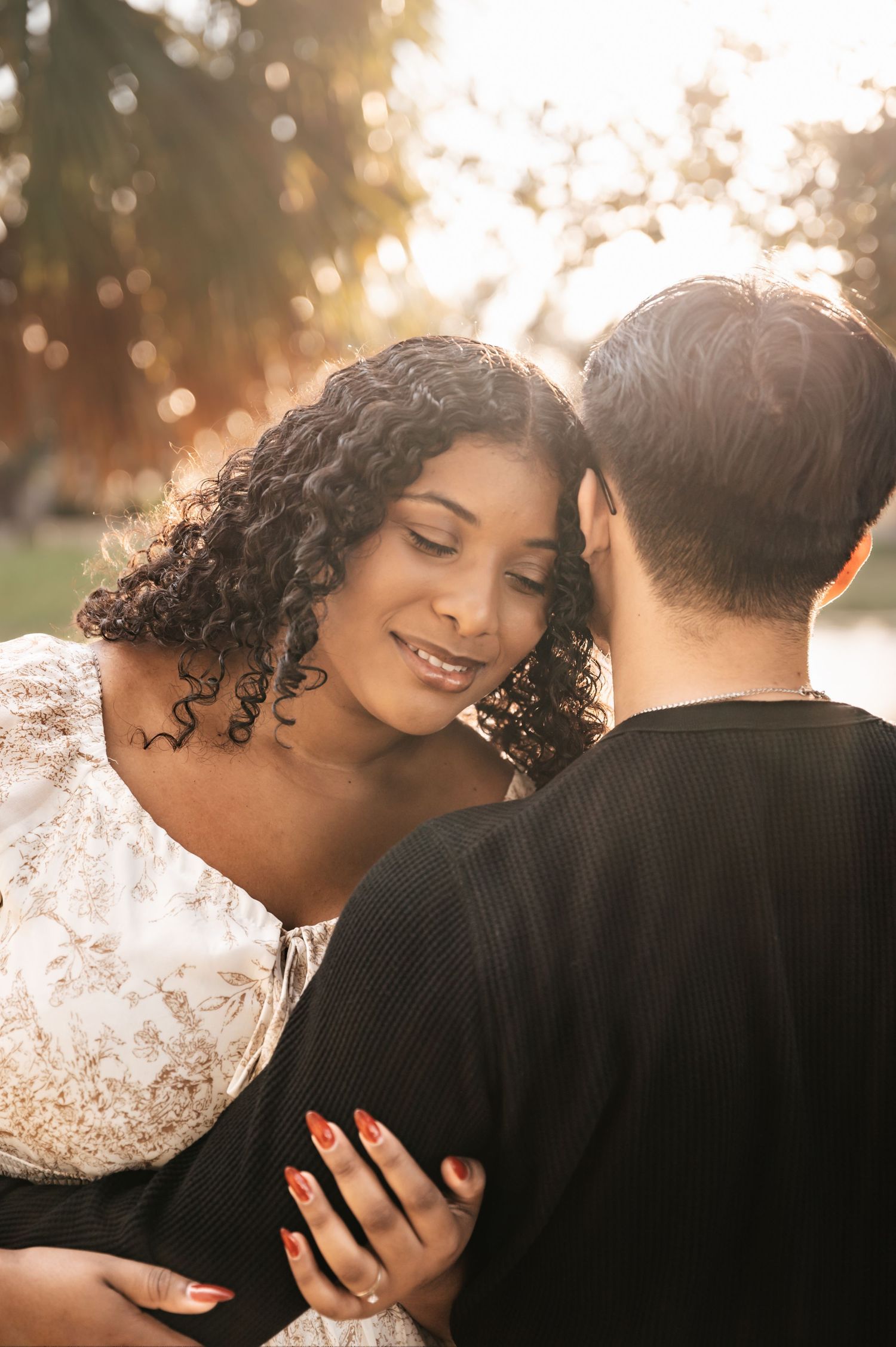 A romantic couple embraces in golden sunlight wearing black and white attire during an intimate outdoor photoshoot.