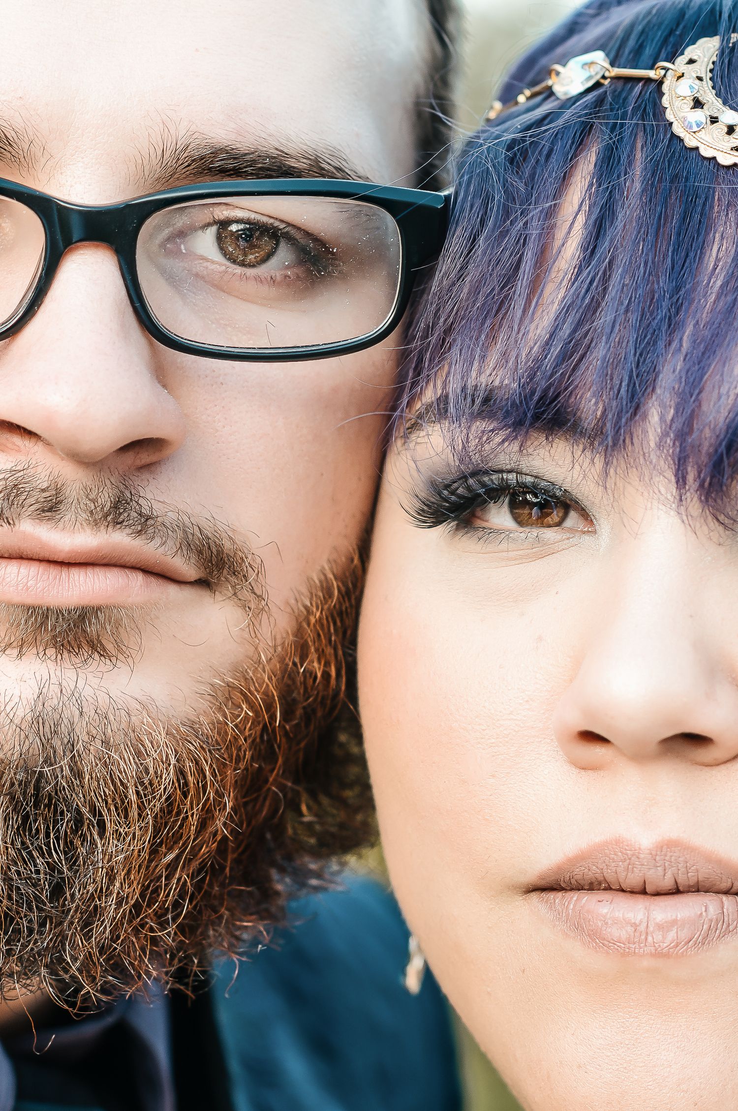 Close-up portrait of a bearded man with glasses and a woman with purple hair and decorative headpiece.