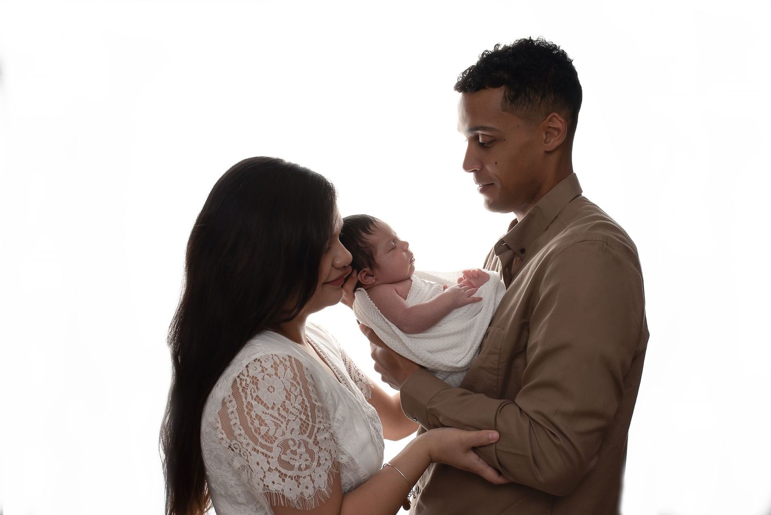 Family wearing white and brown outfits poses together against white backdrop in studio setting.