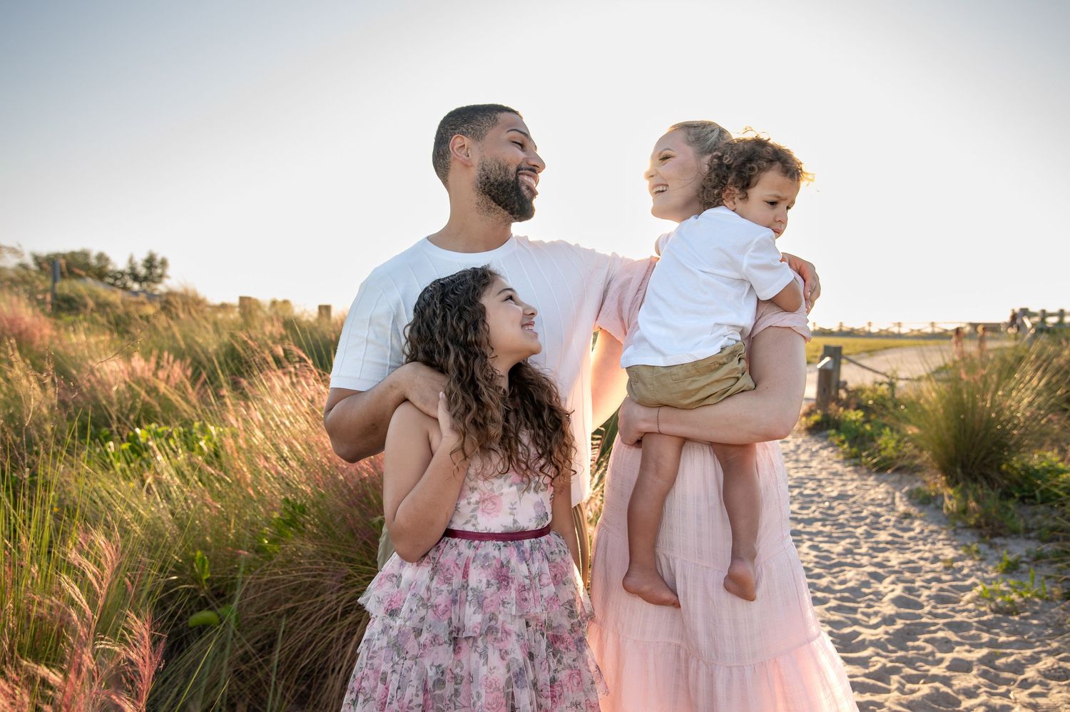 Family photoshoot at sunset on a beach path with tall grass and warm lighting.