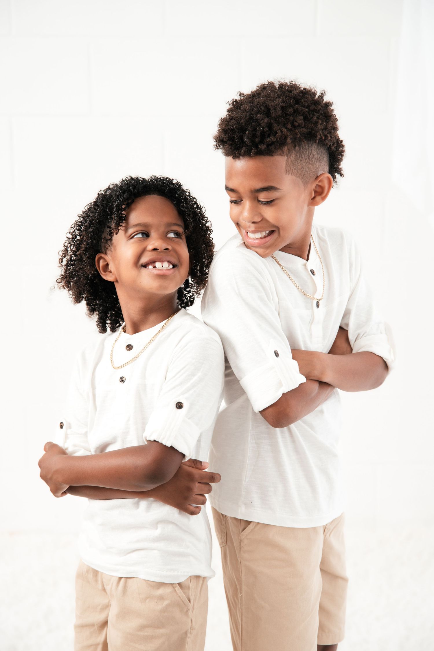 Two children in matching white polos and khaki shorts share joyful laughter against white background.