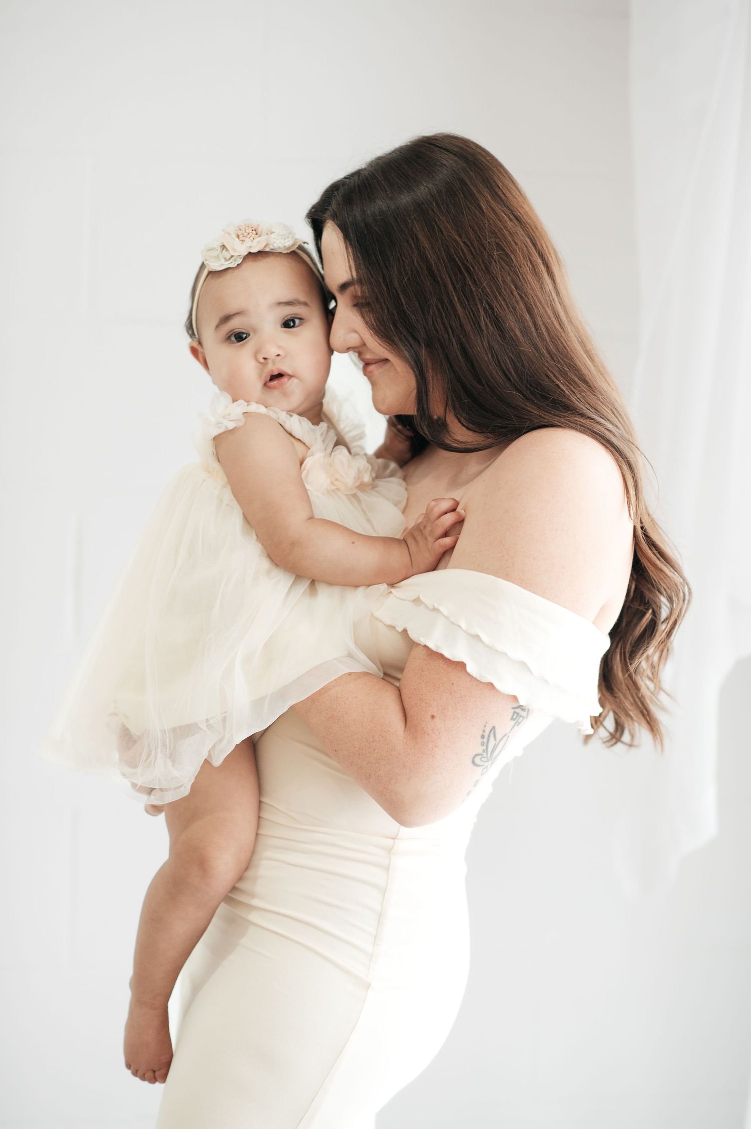 Mother and baby in matching white outfits during intimate studio photoshoot.