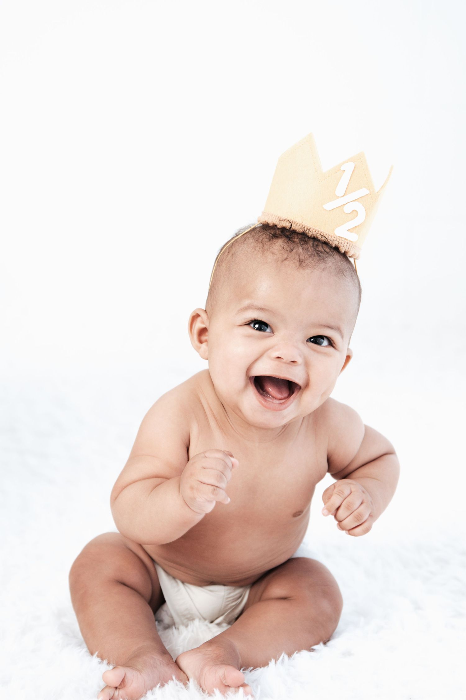 Happy baby wearing diaper lying on white blanket with joyful expression.