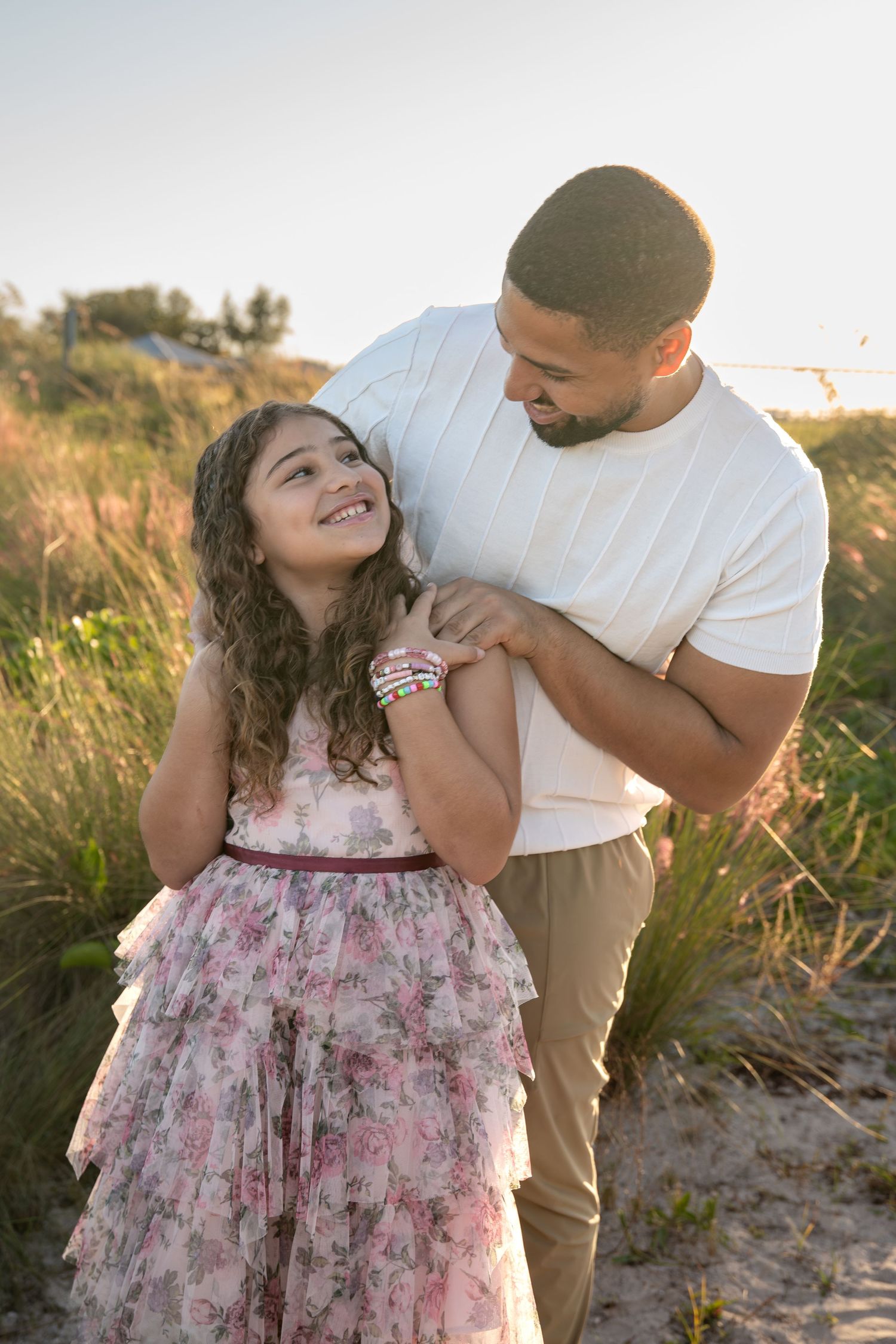A parent and child share a tender moment together at sunset on a beach with tall grass in the background.