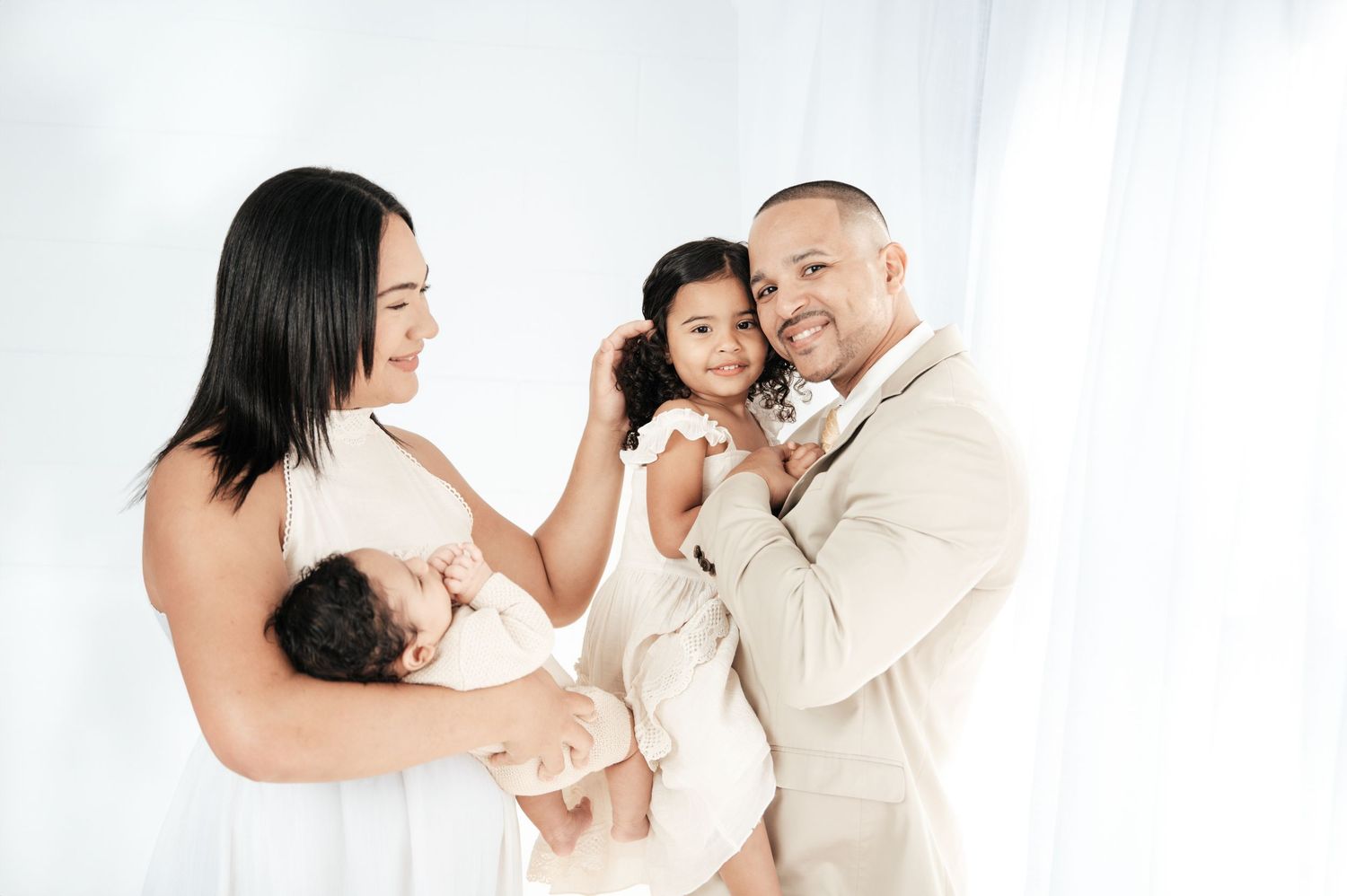 Professional family photo session with everyone dressed in white against a bright studio background.