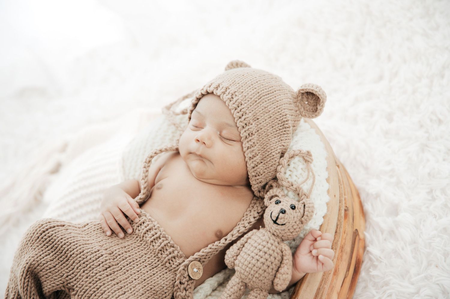Baby in knitted beige outfit sleeping in rustic basket.