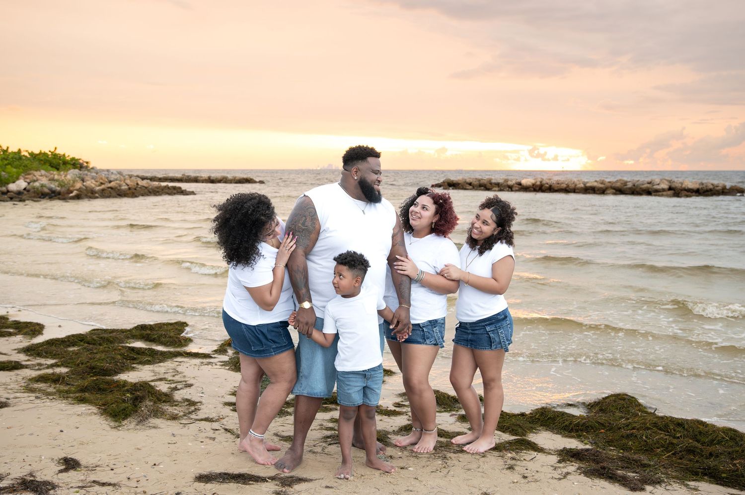 Family wearing coordinated white and denim outfits on beach at sunset.