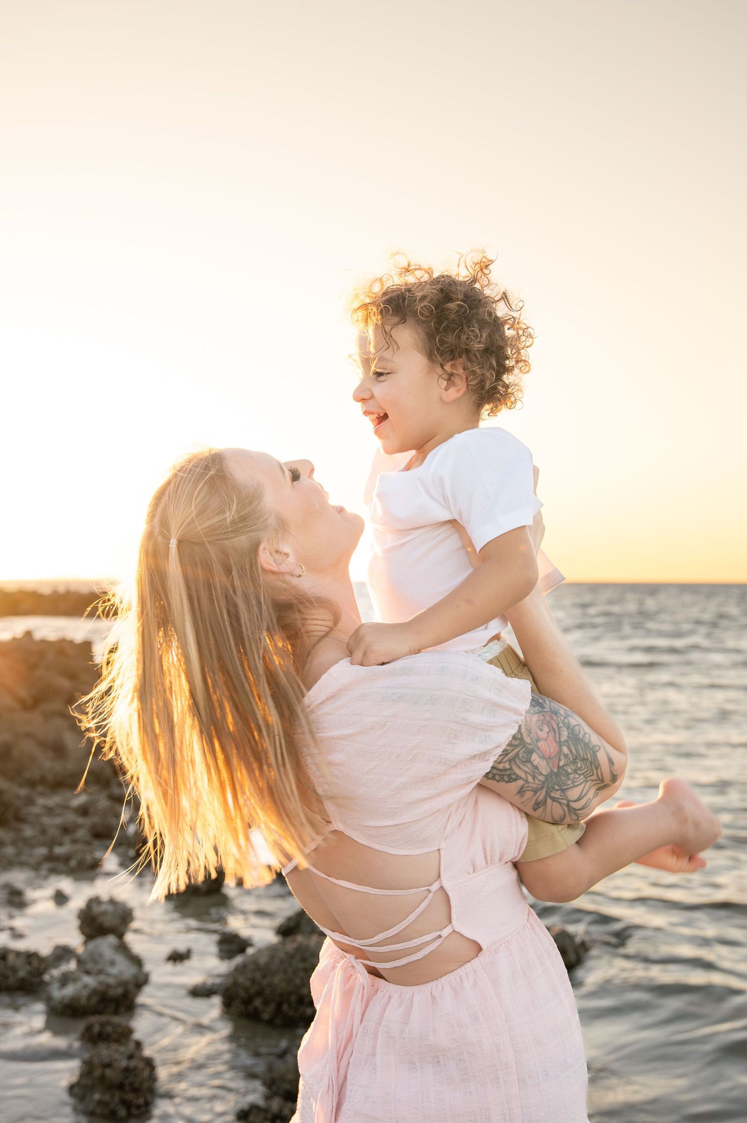 A tender moment shared between parent and child playing together at sunset by the rocky ocean shore.