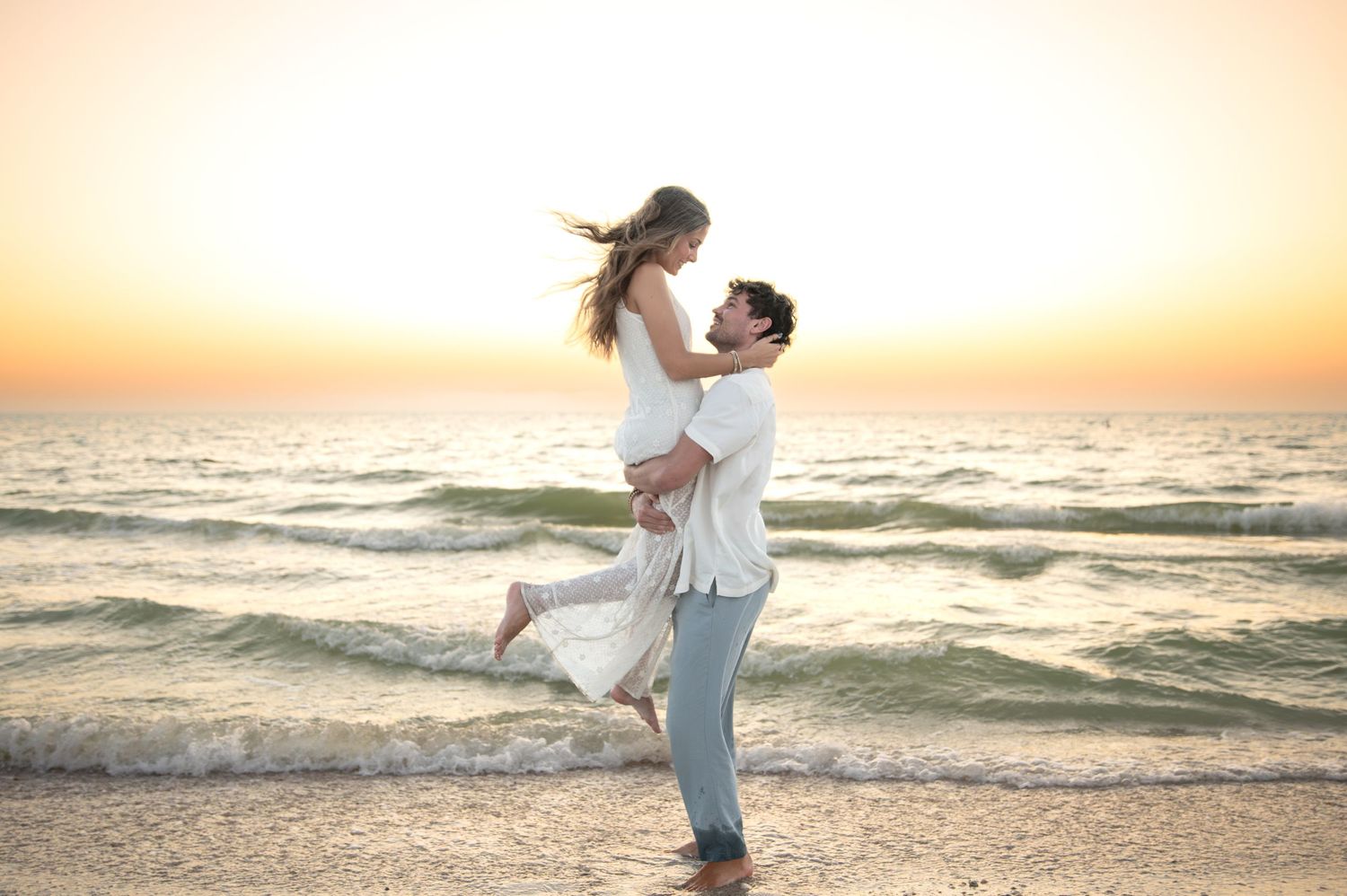 Romantic beach photoshoot at sunset with couple embracing by the ocean.