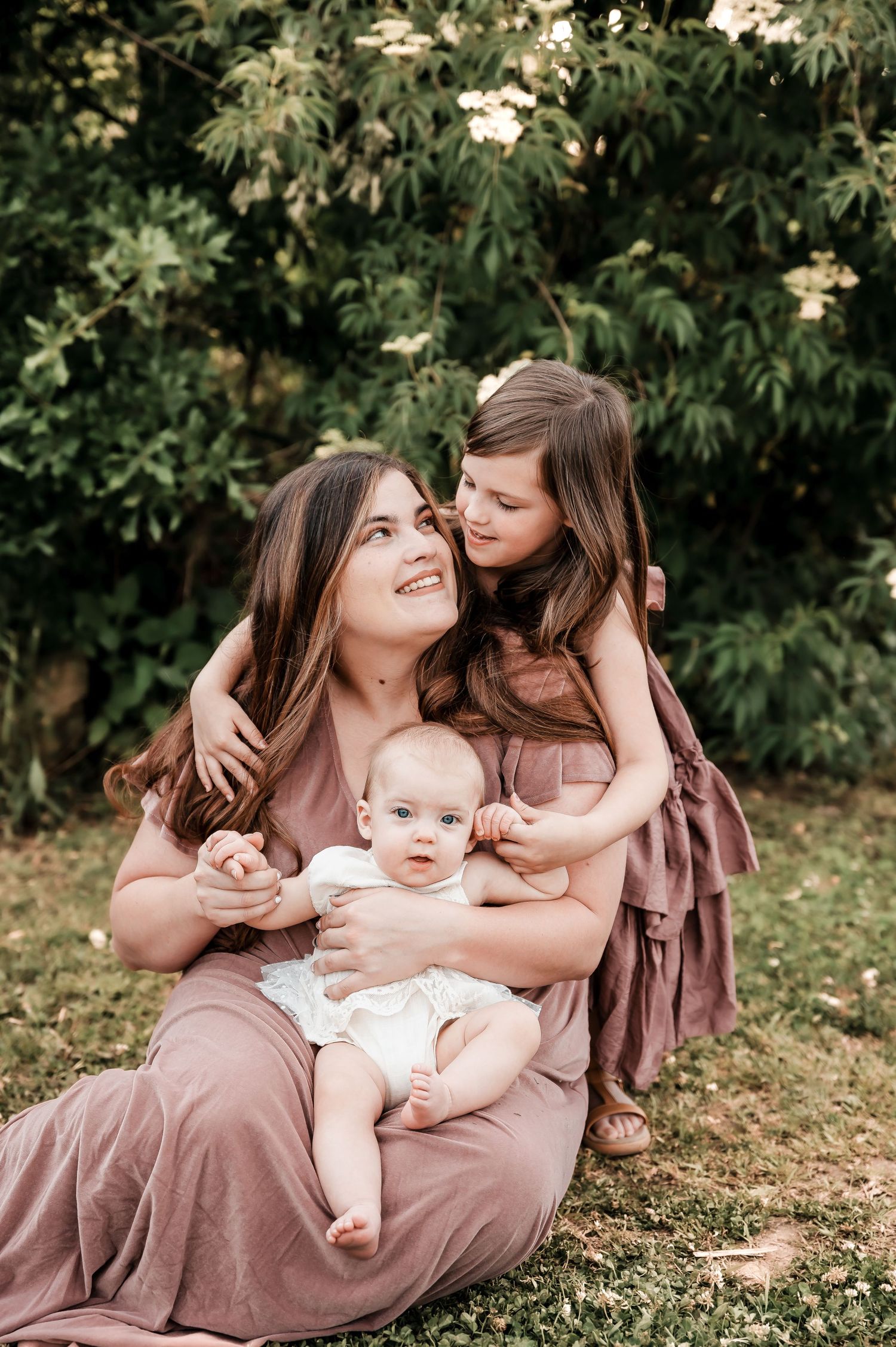 Outdoor family portrait session featuring coordinated mauve dresses in a natural garden setting.