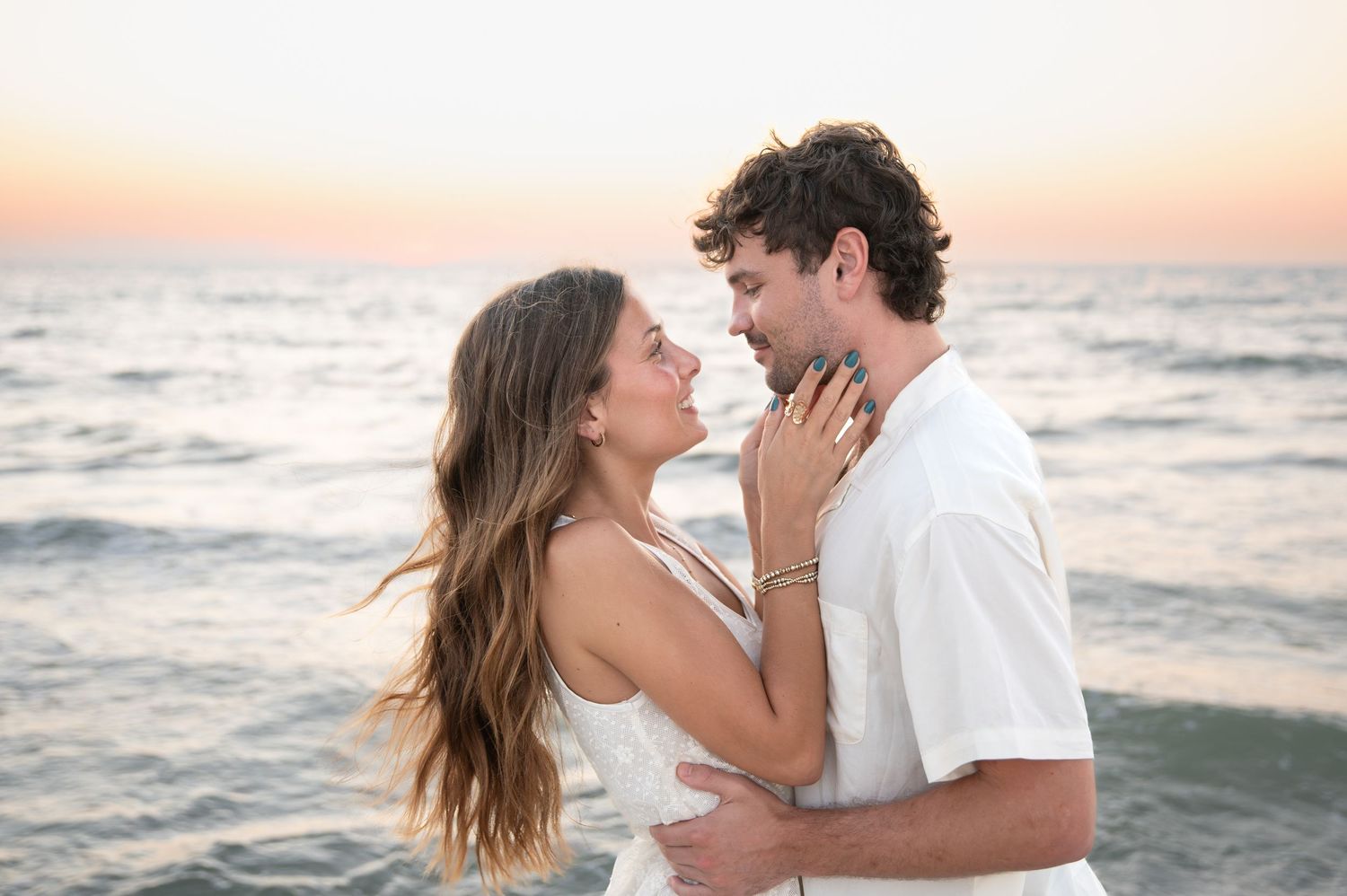 Romantic beach photoshoot of couple embracing at sunset by the ocean.
