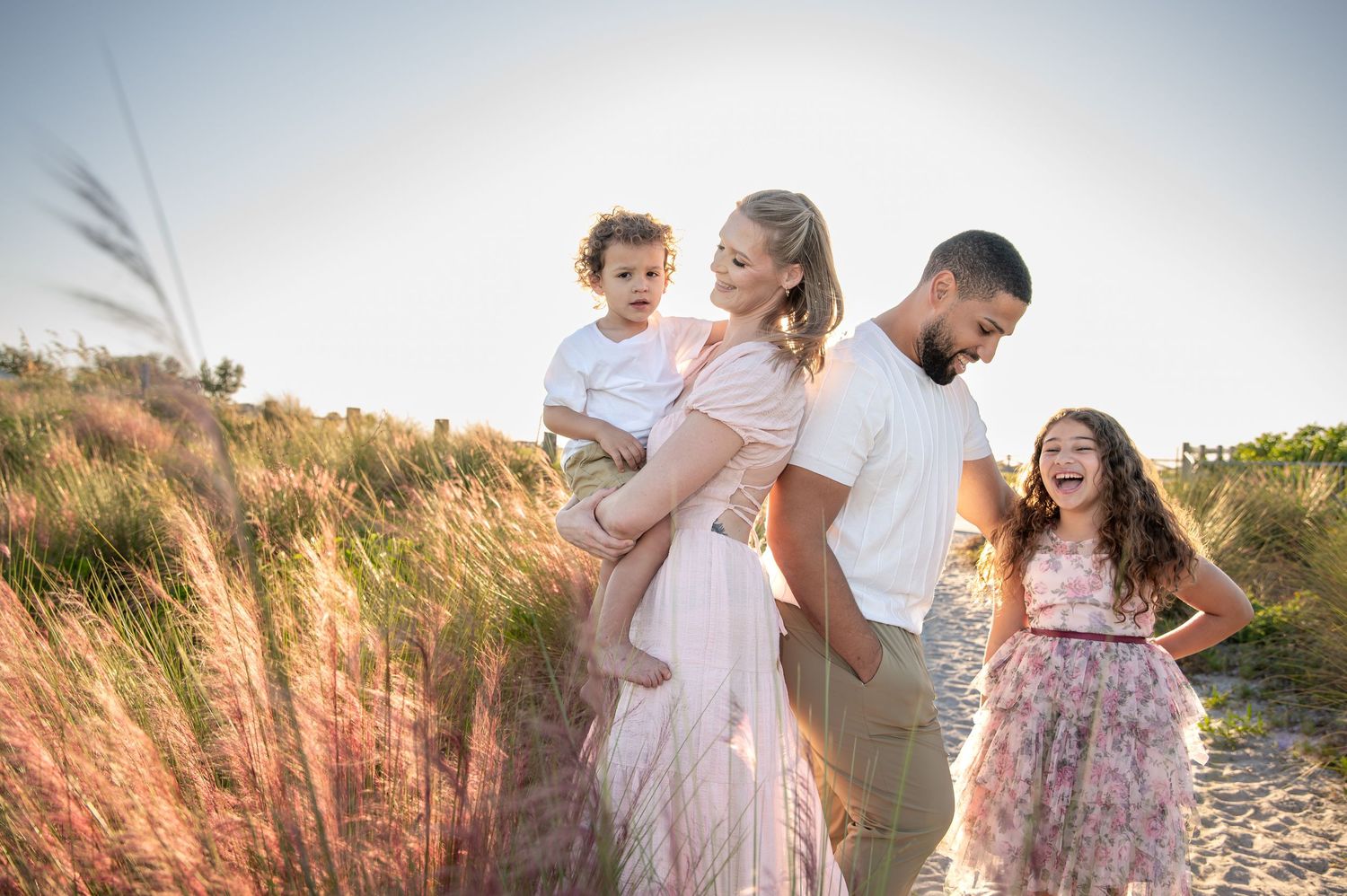 A family shares joyful moments together in a golden field during sunset, wearing light colored outfits.