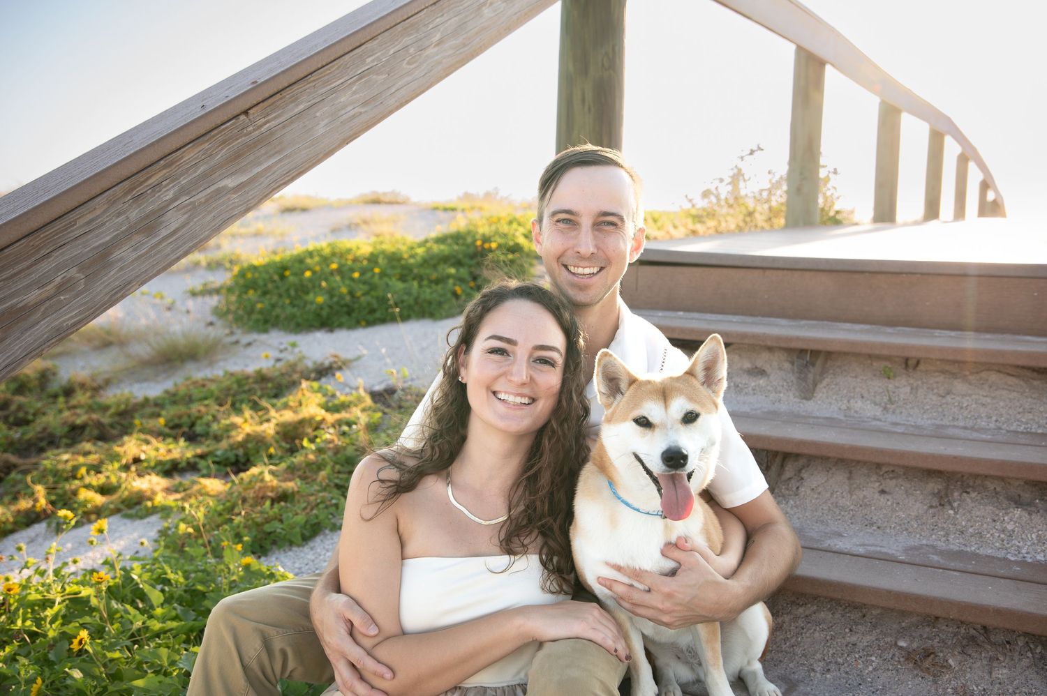 Family portrait session at beach boardwalk with pet dog at sunset.