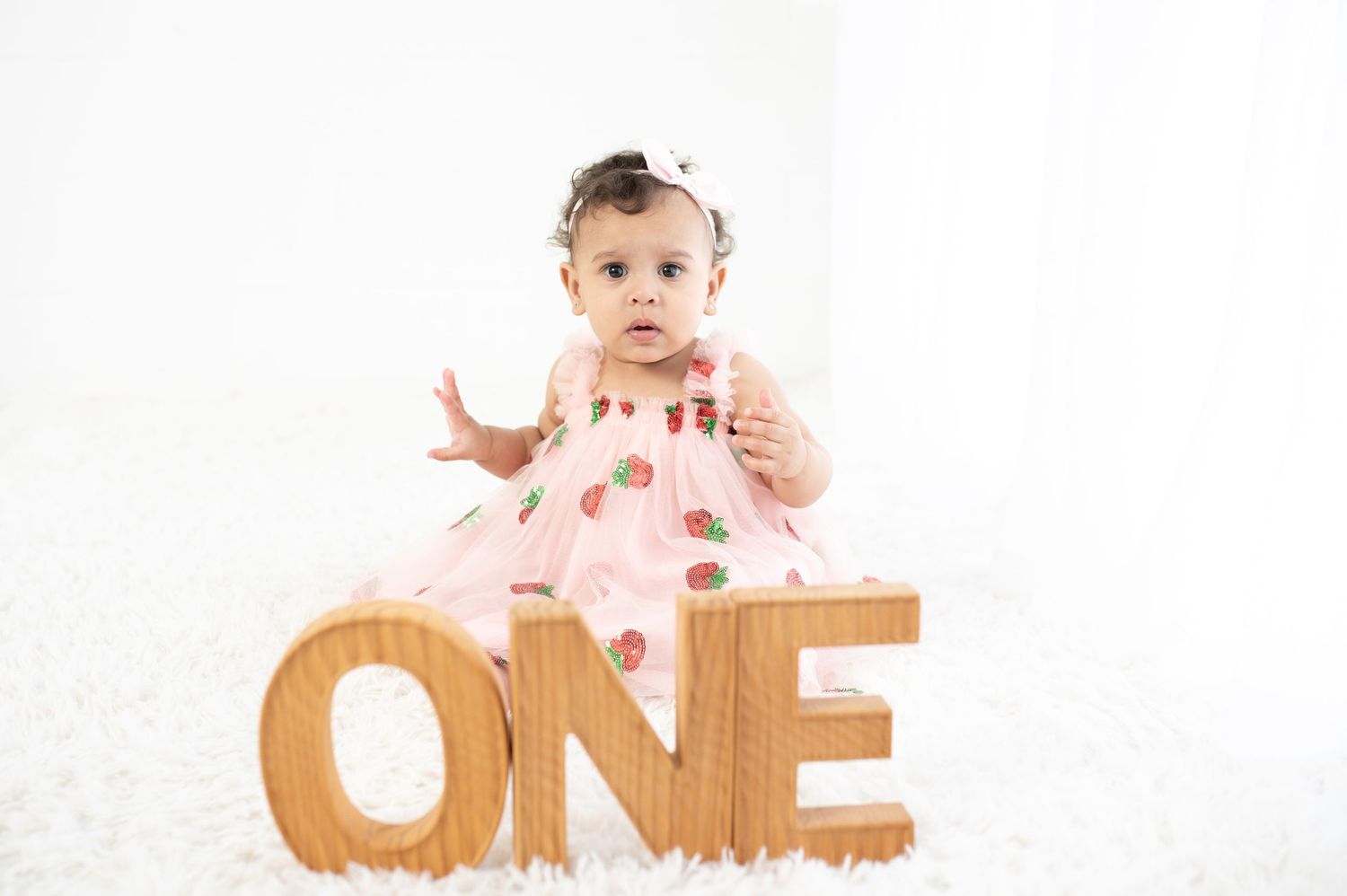 Baby in pink outfit posing with wooden ONE letters for birthday photoshoot.