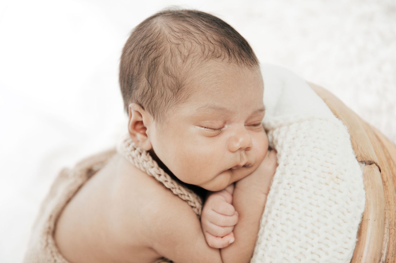 A sleeping newborn baby rests peacefully on soft white blankets.