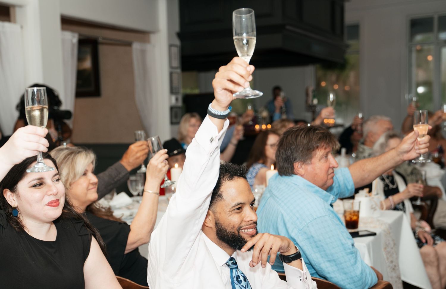 Wedding guests raising glasses during reception celebration at indoor venue.