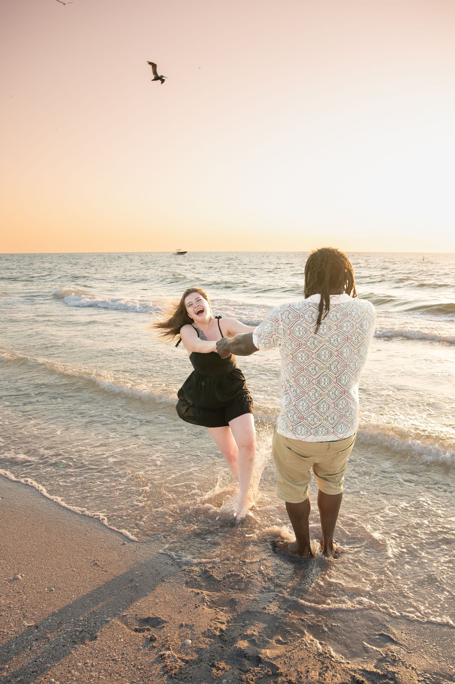 Couple walking along shoreline during golden hour sunset at the beach.