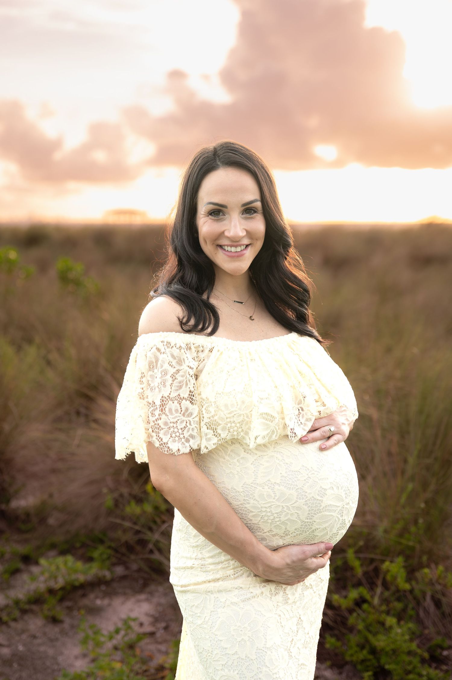 Maternity portrait in lace dress during golden sunset in field.