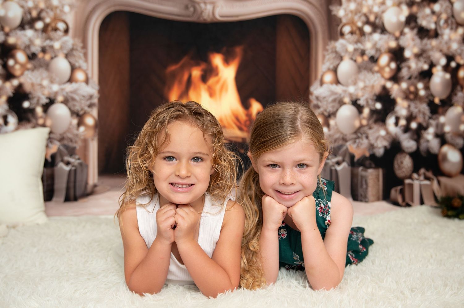 Children smiling in front of decorated Christmas scene with fireplace.