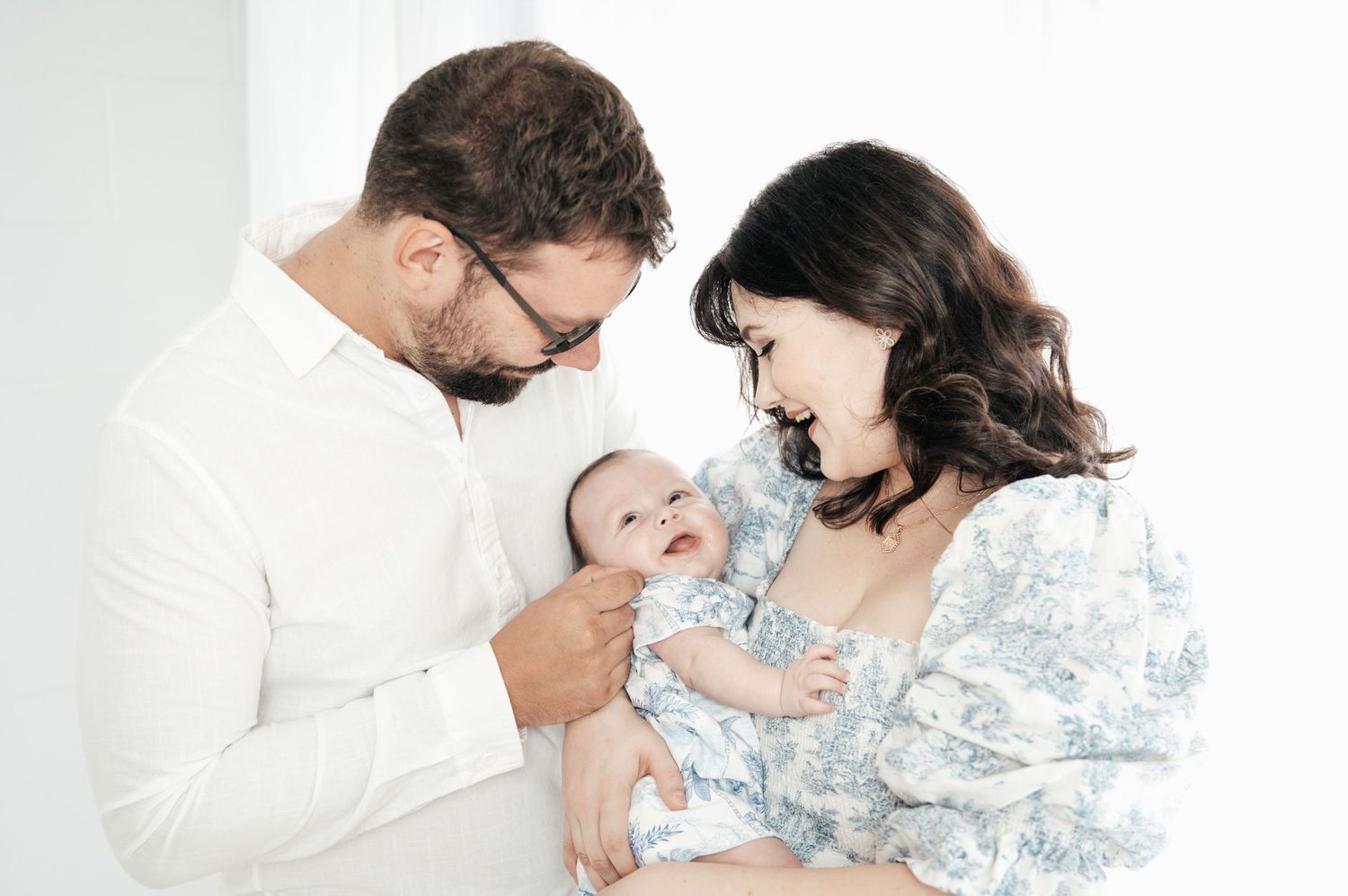 Intimate family portrait session with parents and baby in soft blue and white tones.