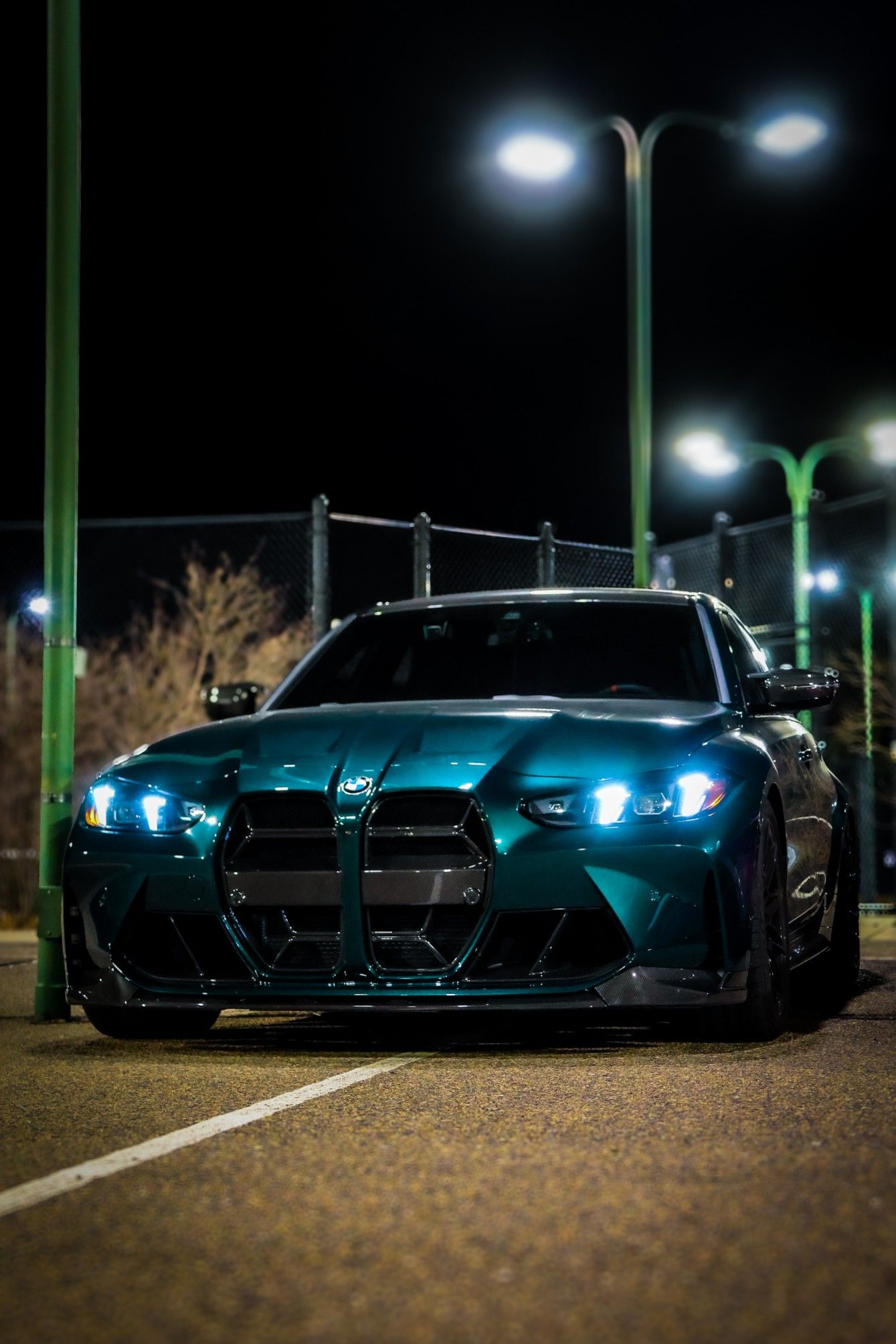 A row of modern BMW M4 sports cars with glowing blue headlights parked at night under illuminated street lamps.