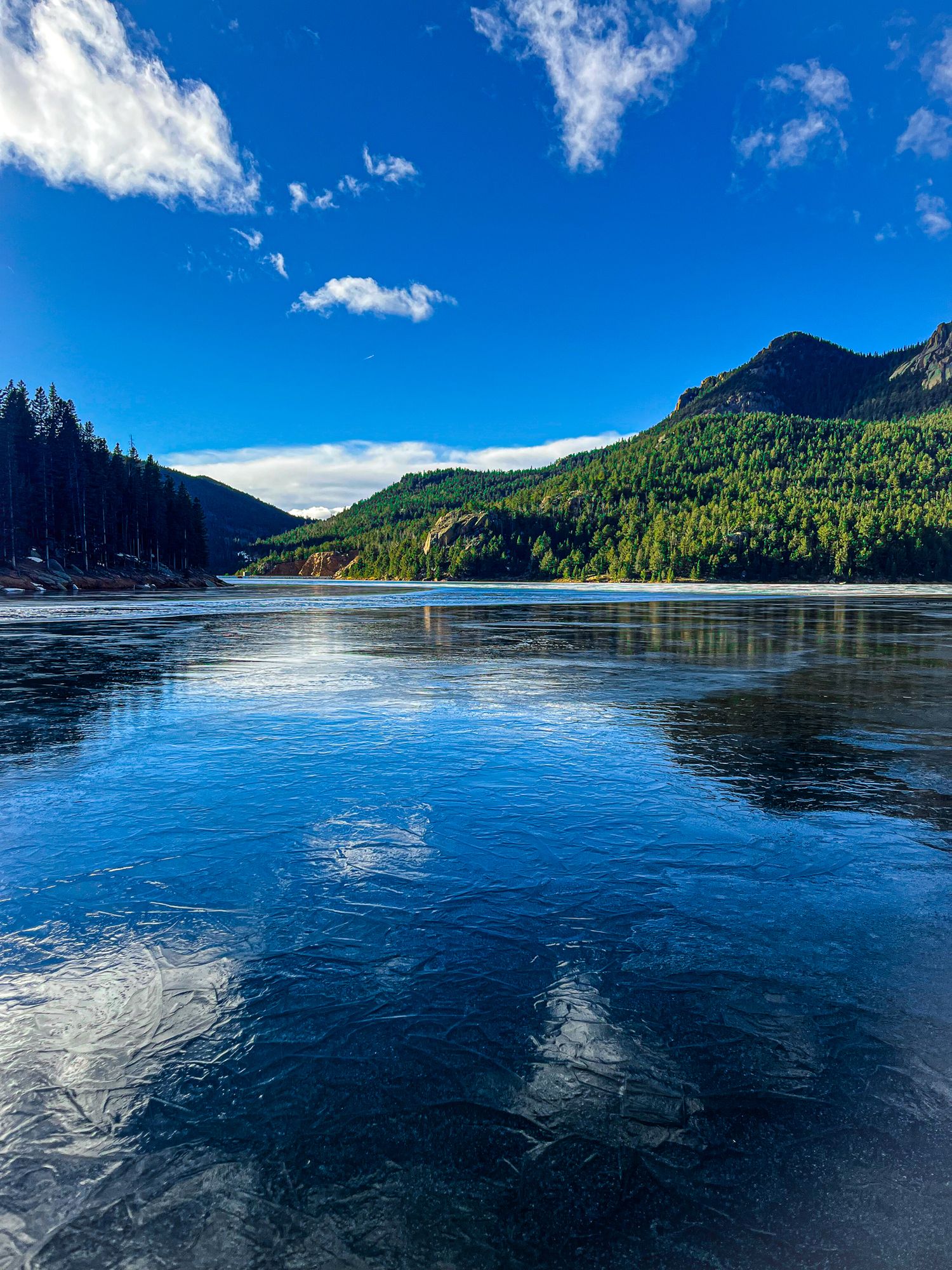 Panoramic sequence of a serene mountain lake with blue waters reflecting clouds and surrounding evergreen forests.