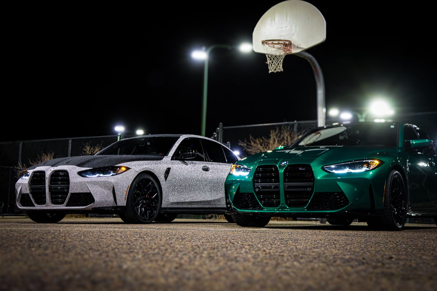 Sports cars parked at night under bright stadium lights with reflective paint glowing in the darkness.