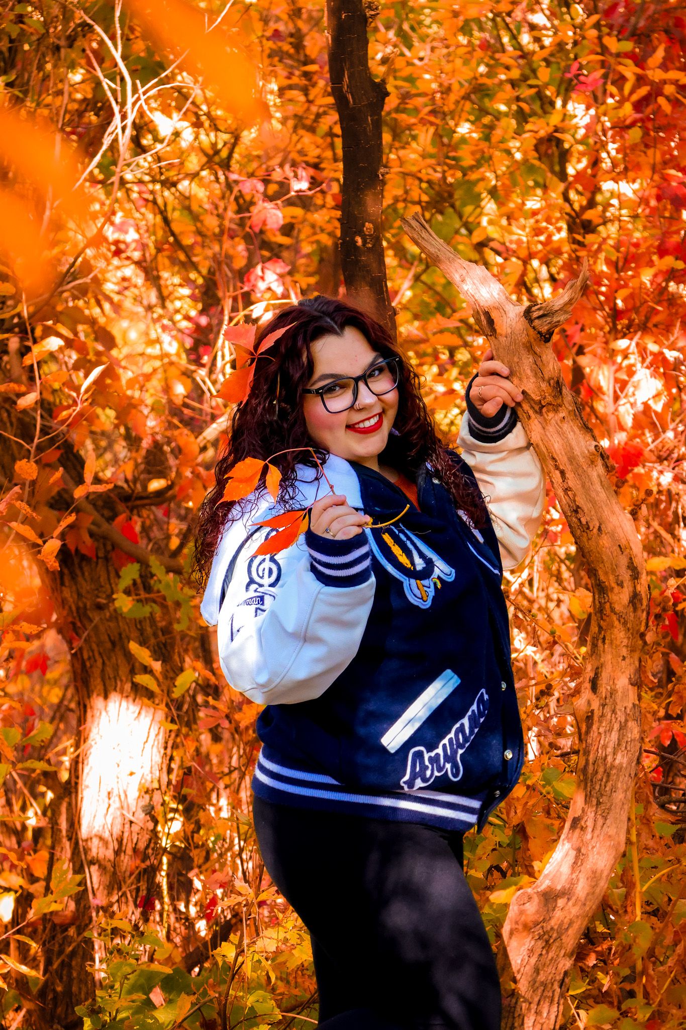Autumn photoshoot featuring varsity jacket poses among vibrant orange fall foliage.