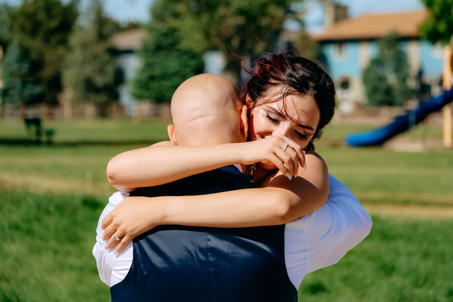A couple embraces in a tender moment on a sunny day in a grassy outdoor setting.