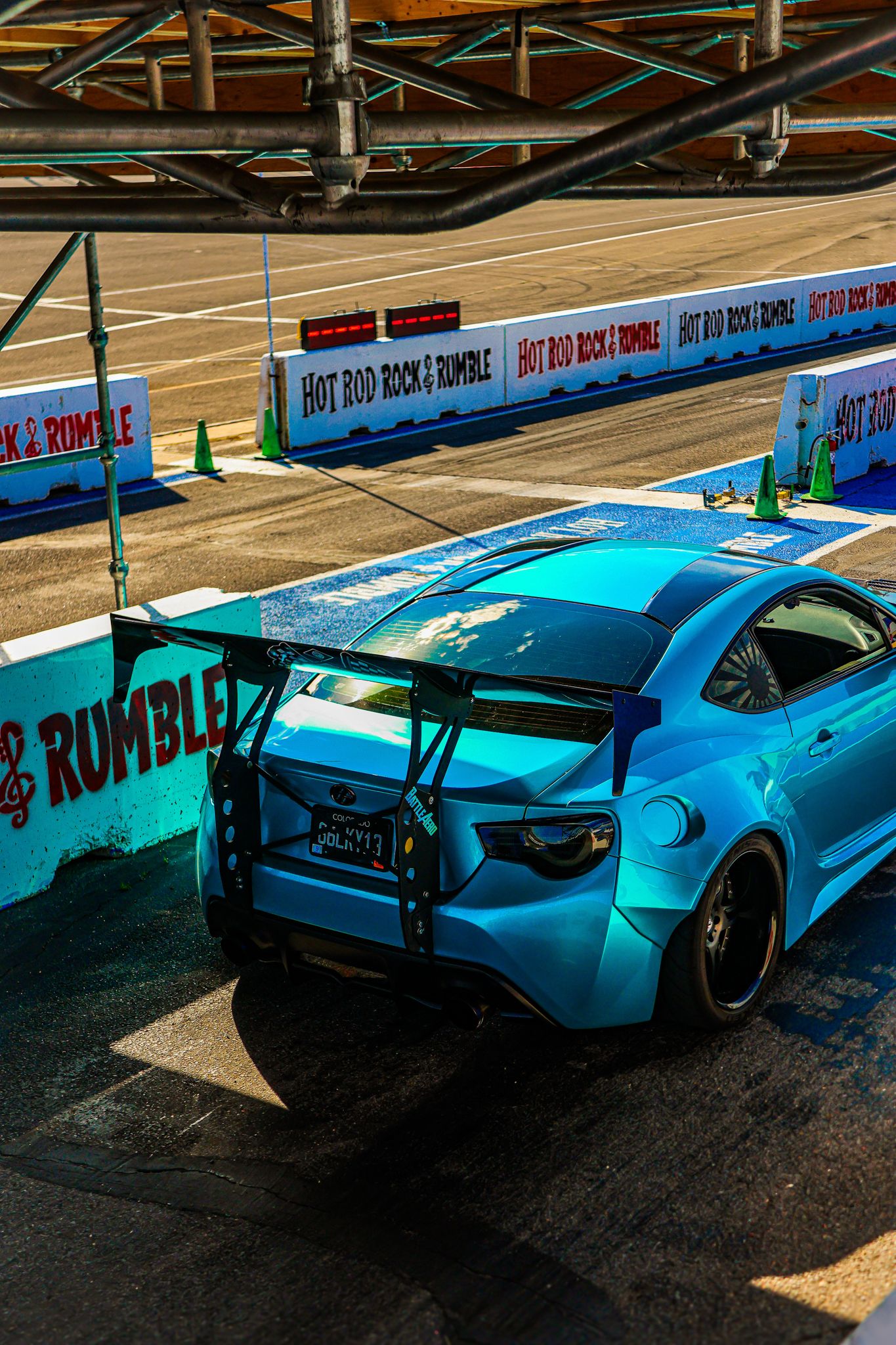 Light blue sports car with wide body kit and custom modifications parked against colorful graffiti wall.