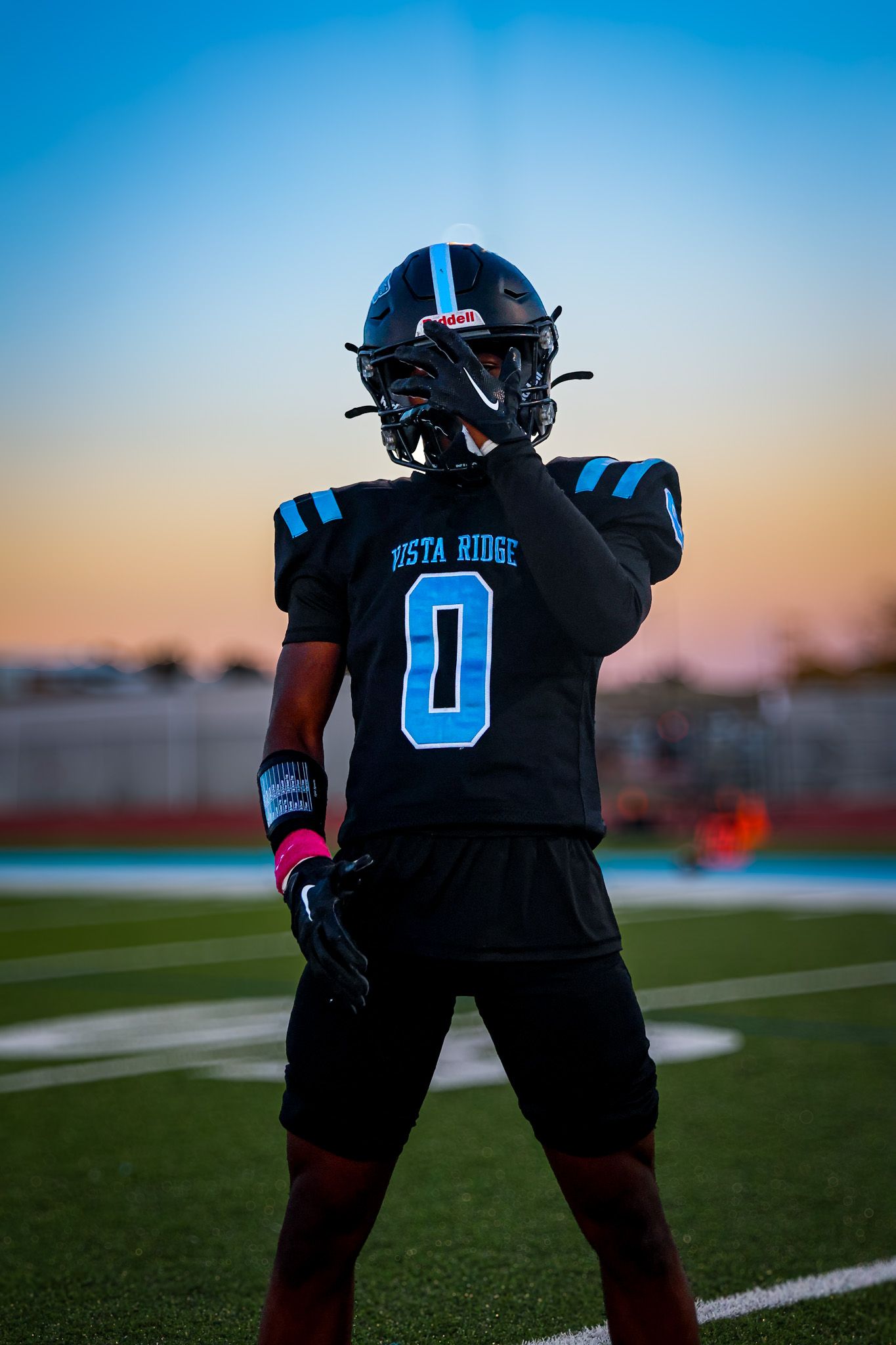 Football player in black uniform with number 0 stands on field during sunset against blue sky.