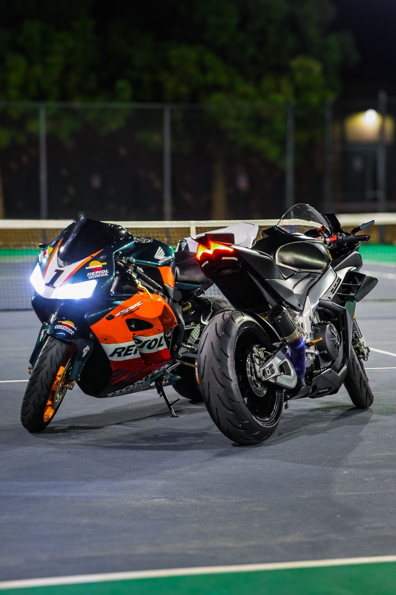 Racing motorcycles lined up in formation on a dark track with Repsol Honda and other sport bikes visible at night.