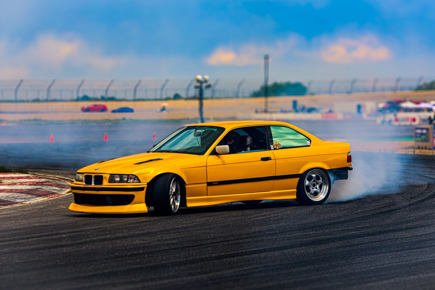 Yellow BMW M3 drifting on a racetrack with smoke coming from the tires during a drift event.