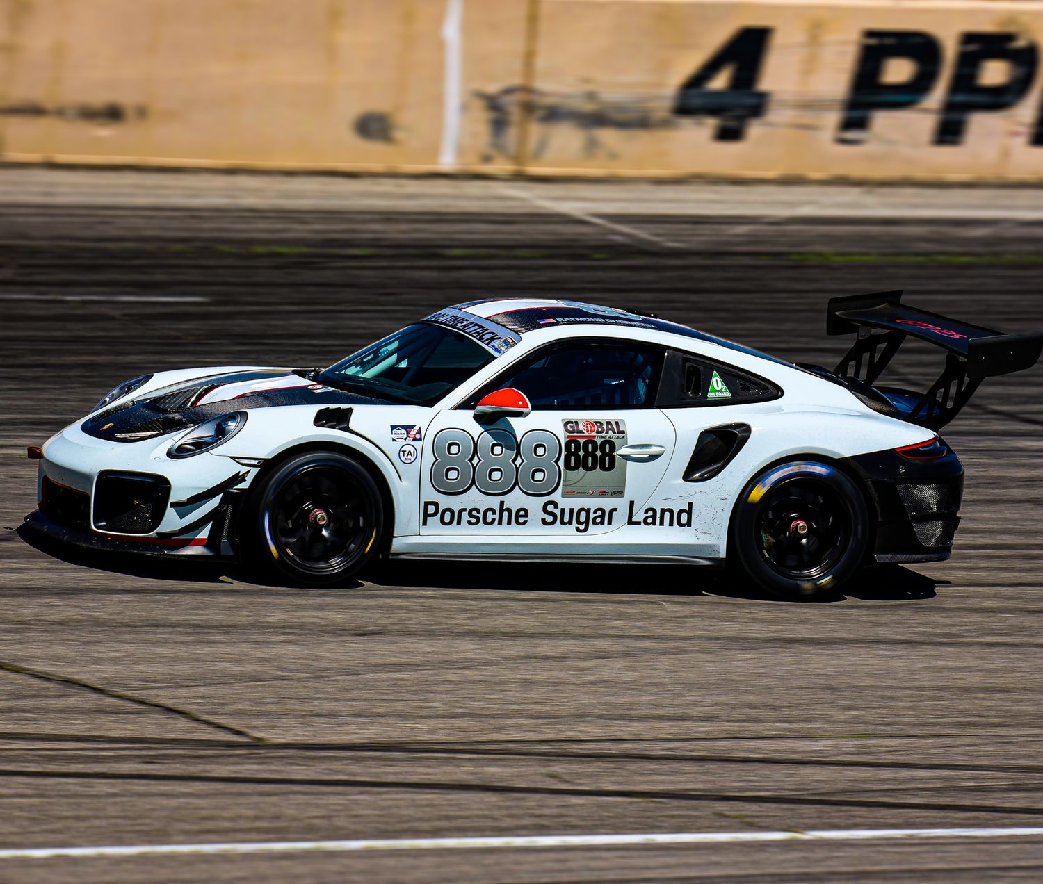Multiple white racing cars with Porsche Sugar Land branding speed along a racetrack during competition.