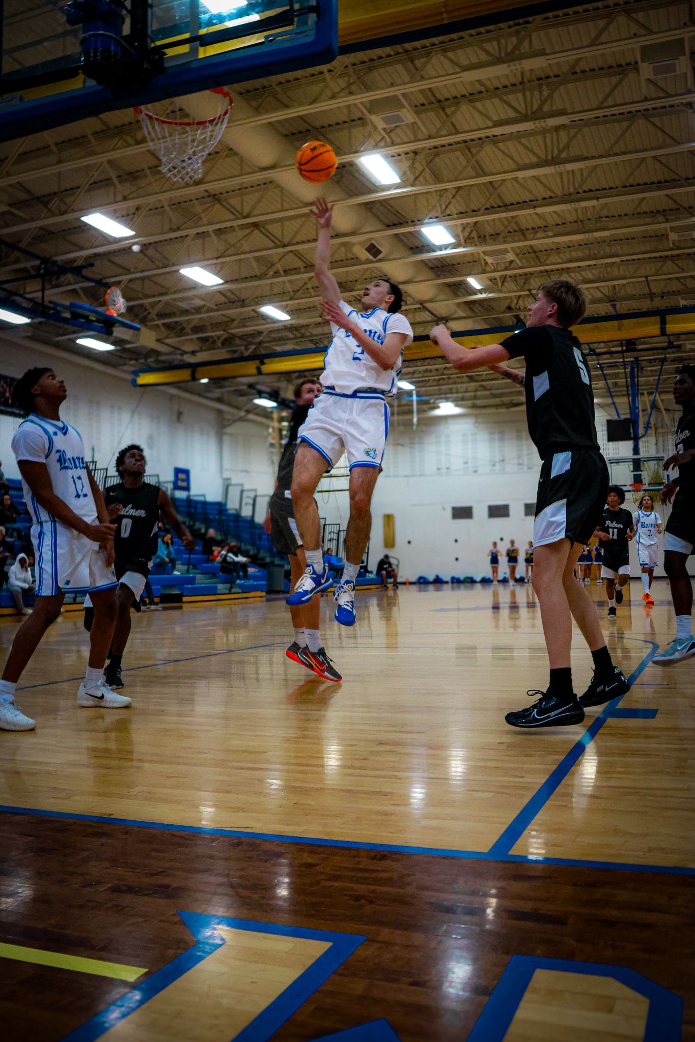 Basketball players leap and stretch across a wooden court during an intense indoor game sequence.