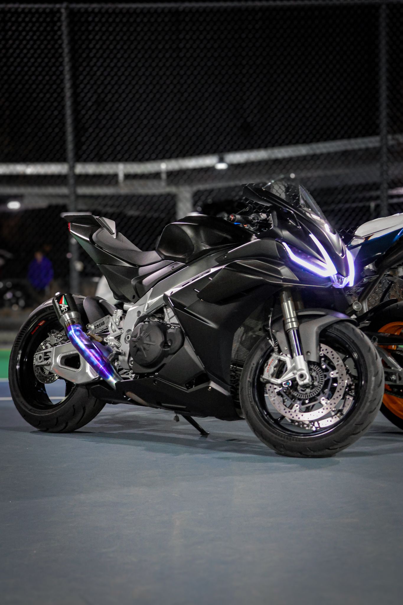 Close-up view of sleek black motorcycles with purple accent lighting lined up in a dark showroom setting.