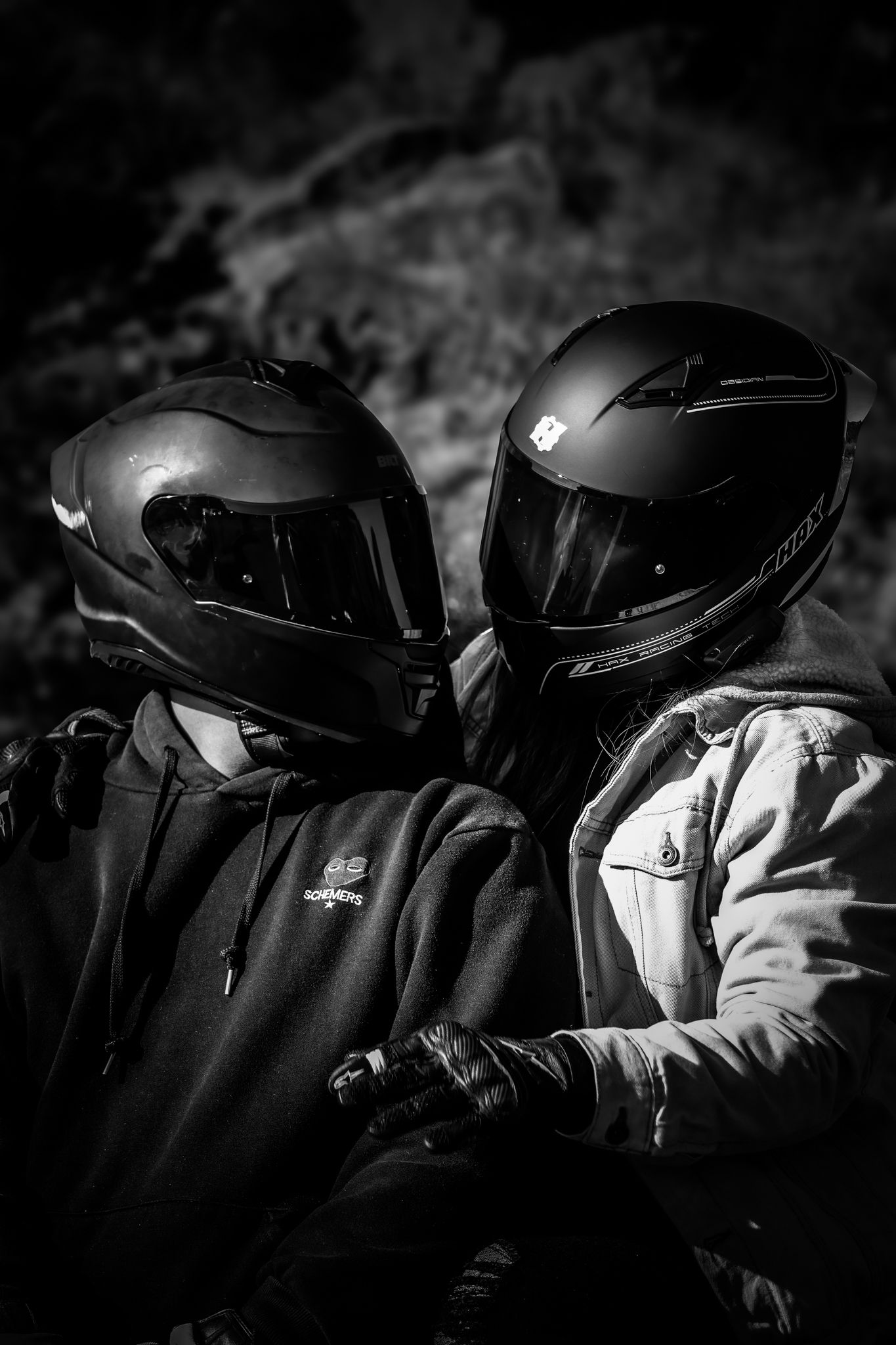 A row of black motorcycle helmets lined up in a dark monochromatic composition showing reflective surfaces.