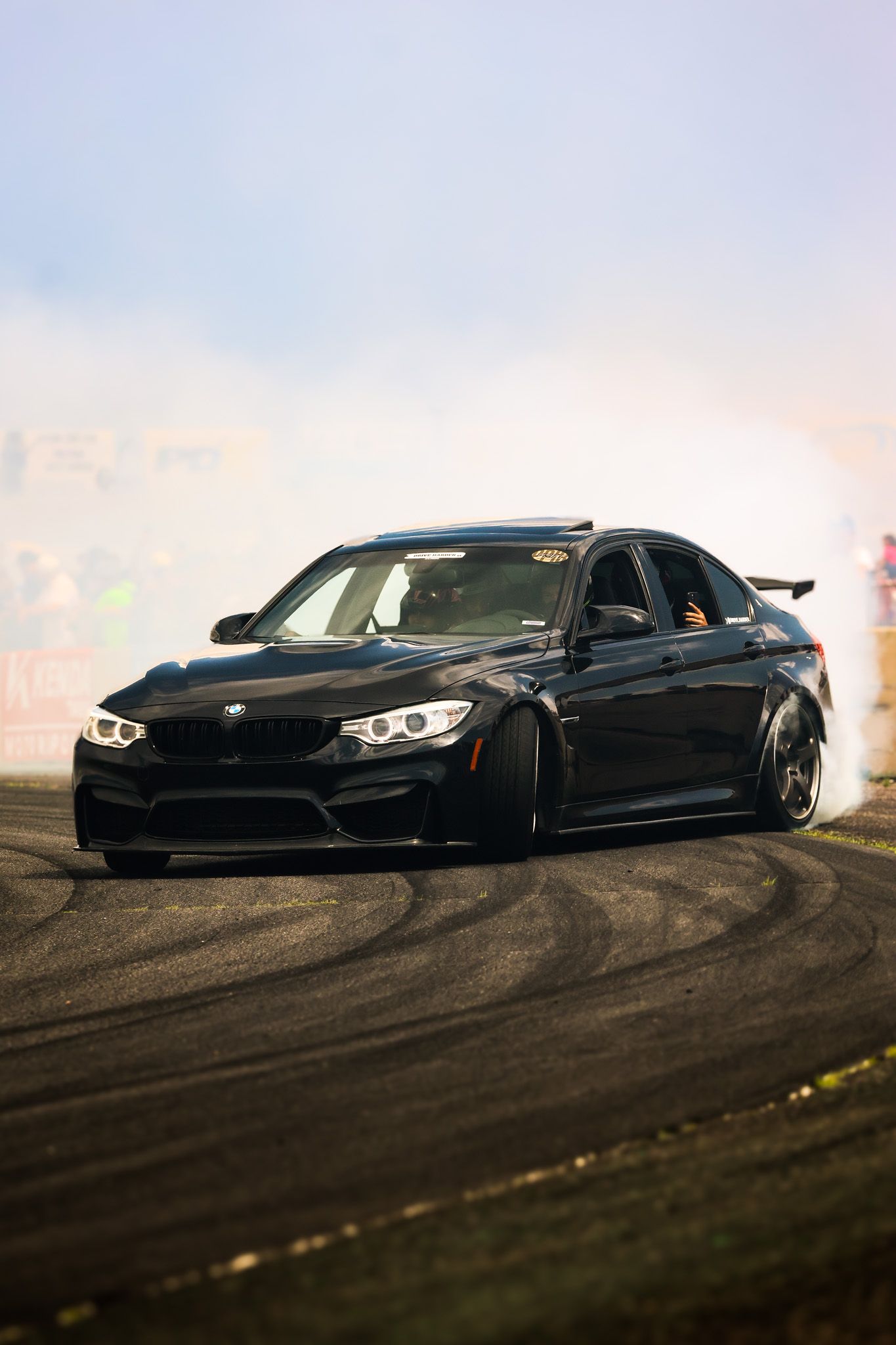 Black BMW M4 drifting on a hillside track against a cloudy sky during sunset.