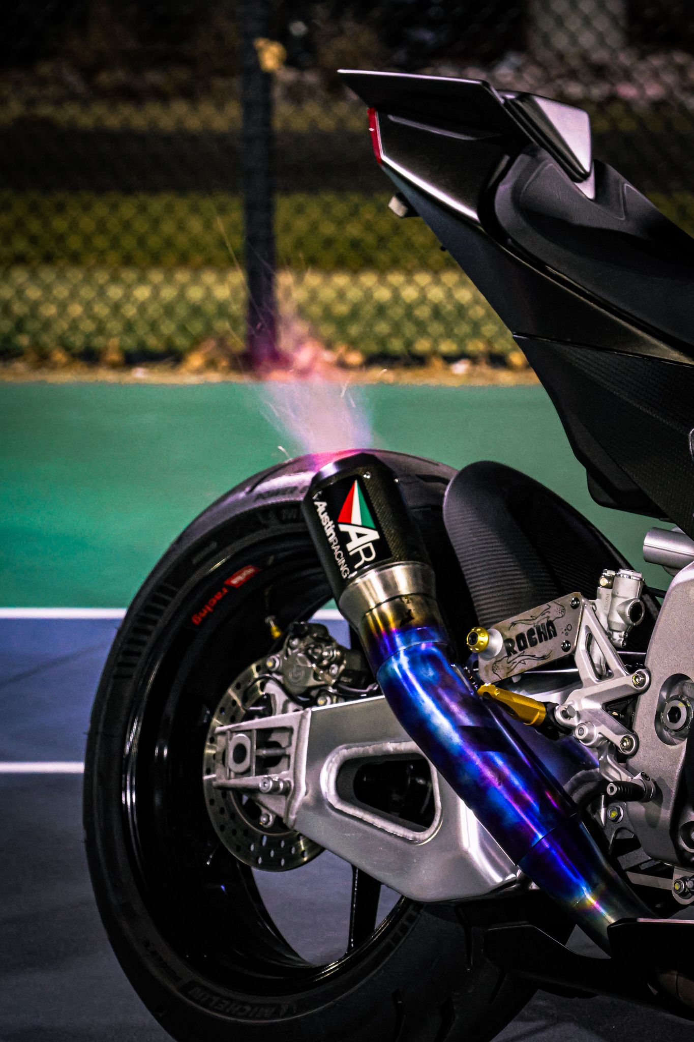 Close-up sequence of a motorcycle's rear suspension and exhaust system with glowing blue and pink lighting effects.