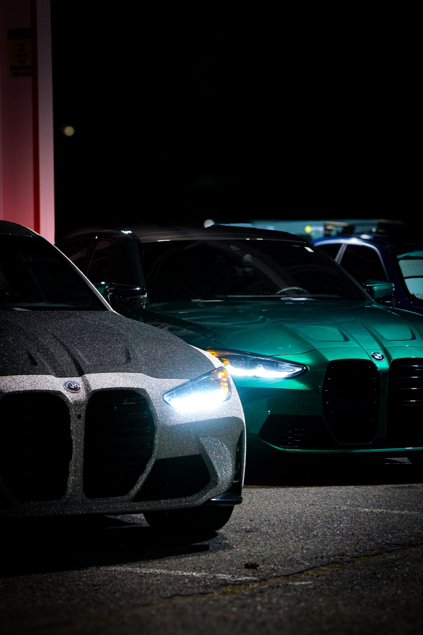 A series of luxury cars in a dark parking lot with dramatic lighting highlighting their sleek silhouettes and glowing headlights.