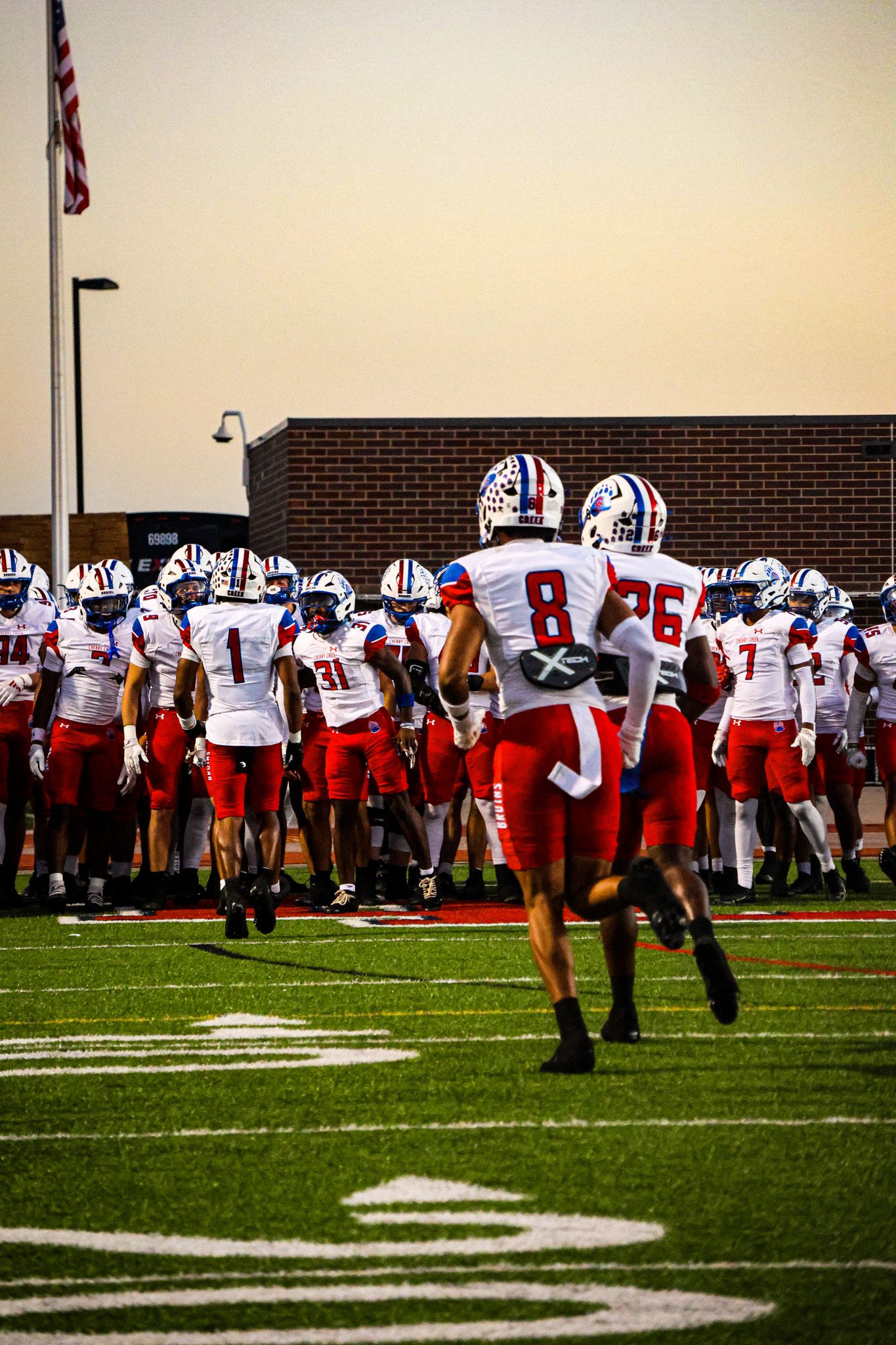 Football players in red and white uniforms practicing on a turf field during a team training session.