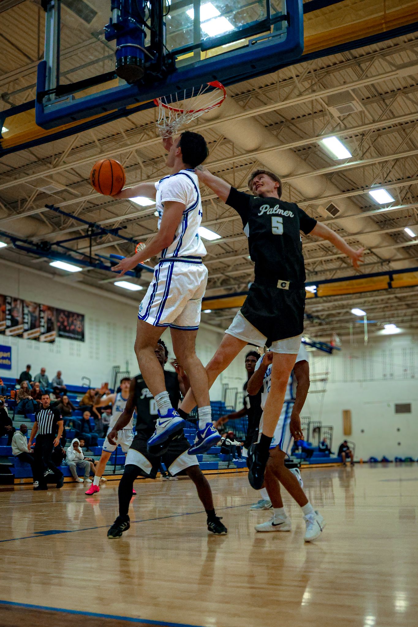 Basketball players compete in an intense game on a wooden court in a gymnasium during a competitive match.