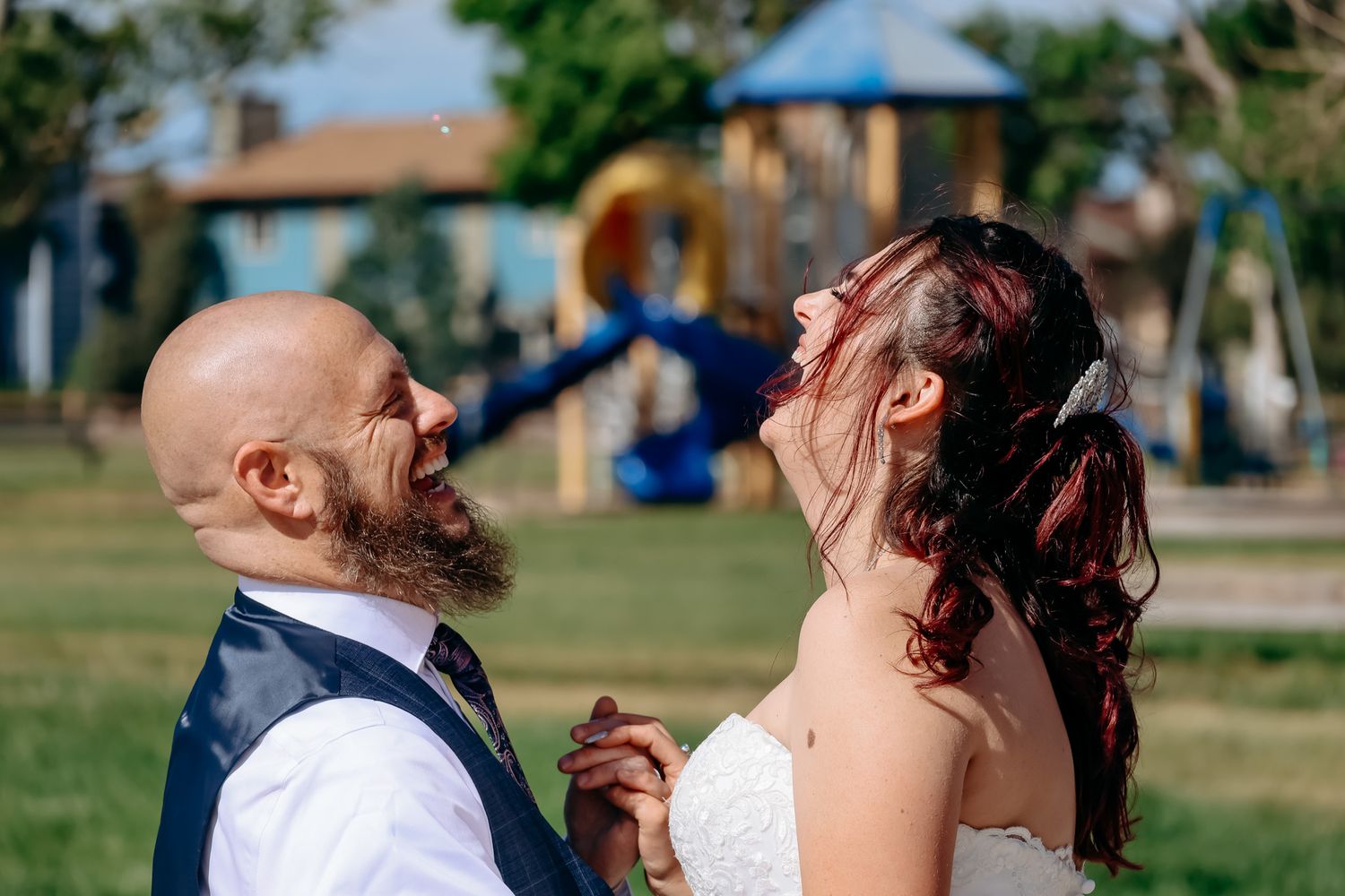 Joyful couple shares a candid laughing moment together outdoors during their wedding celebration.