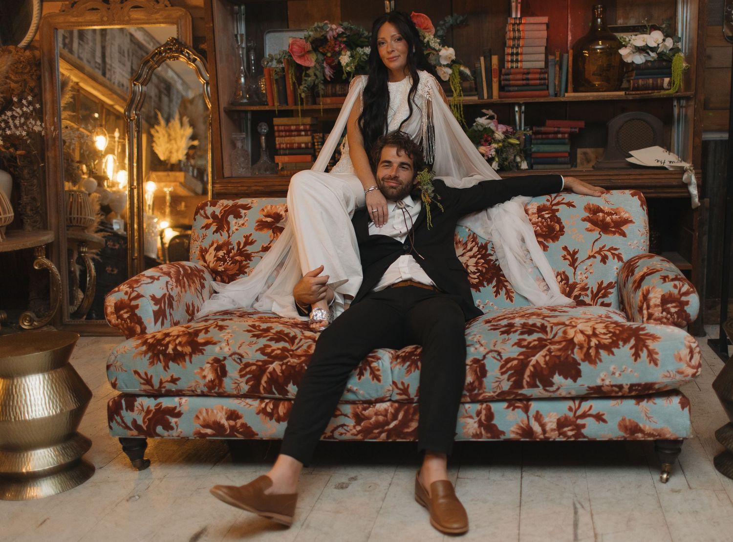 Couple lounging on floral patterned couch in cozy indoor setting.