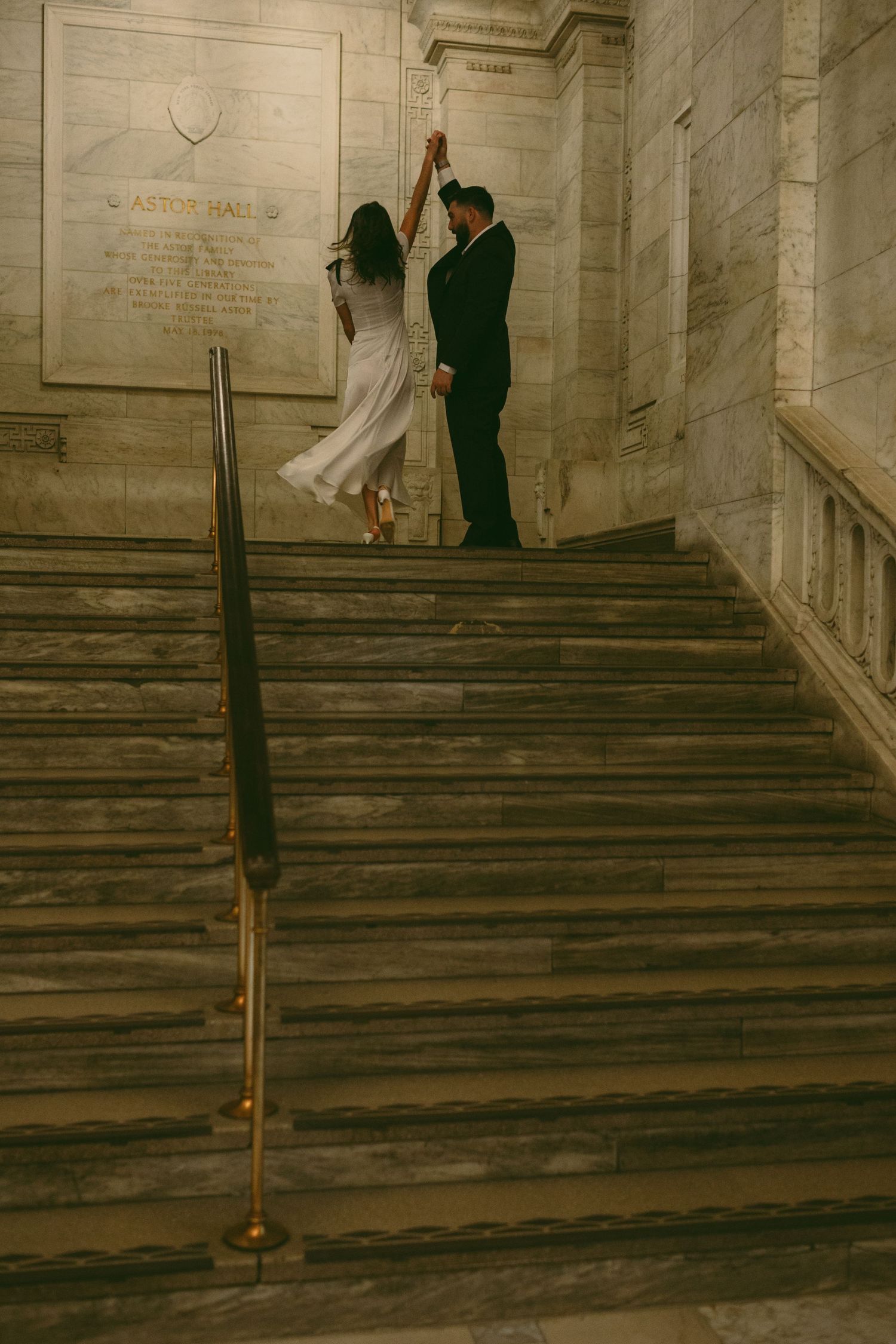 A couple dances on marble stairs in formal wedding attire, creating a romantic vintage-style scene.