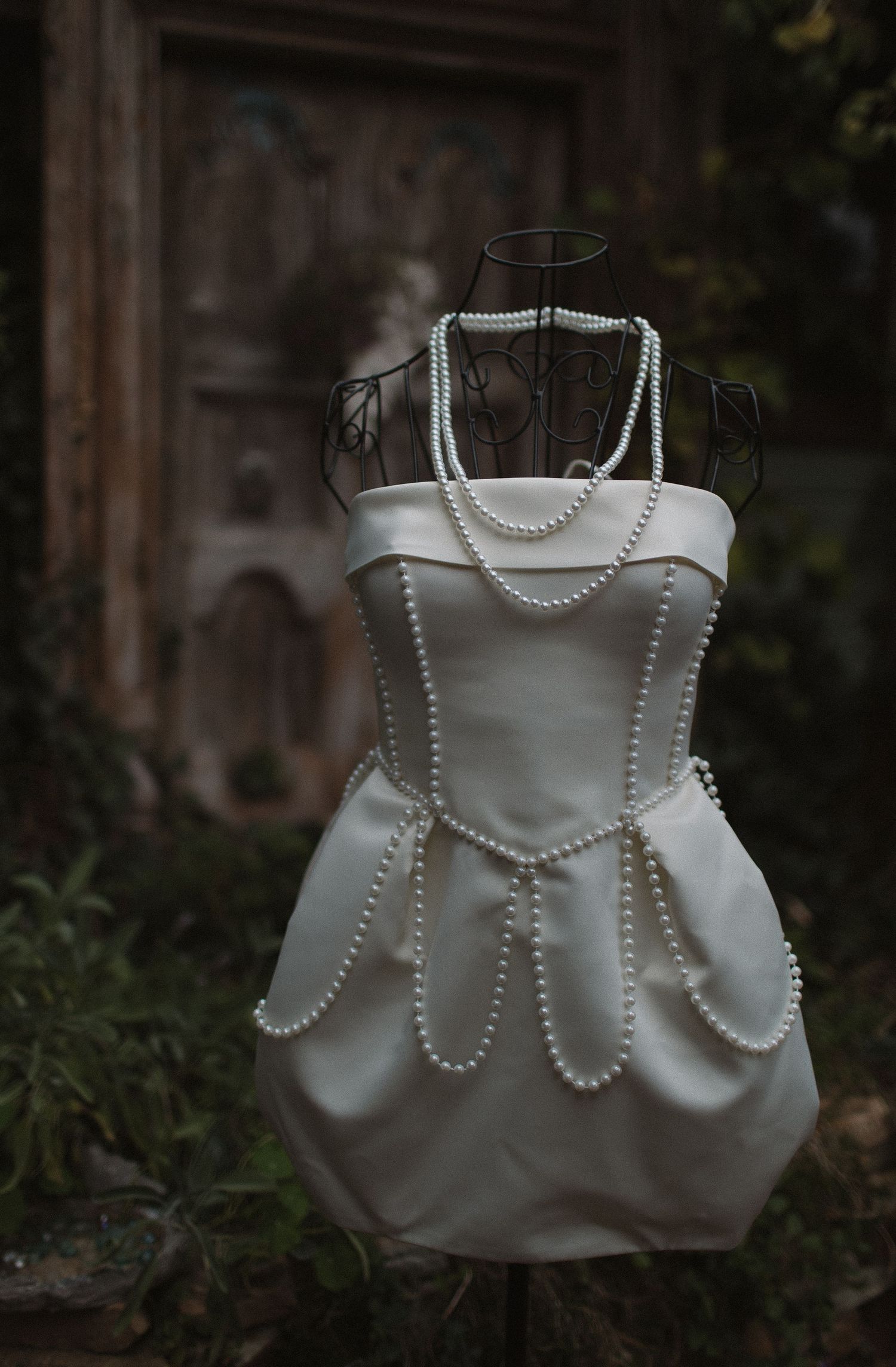 White satin handbag decorated with pearl beading displayed in a dark outdoor setting.