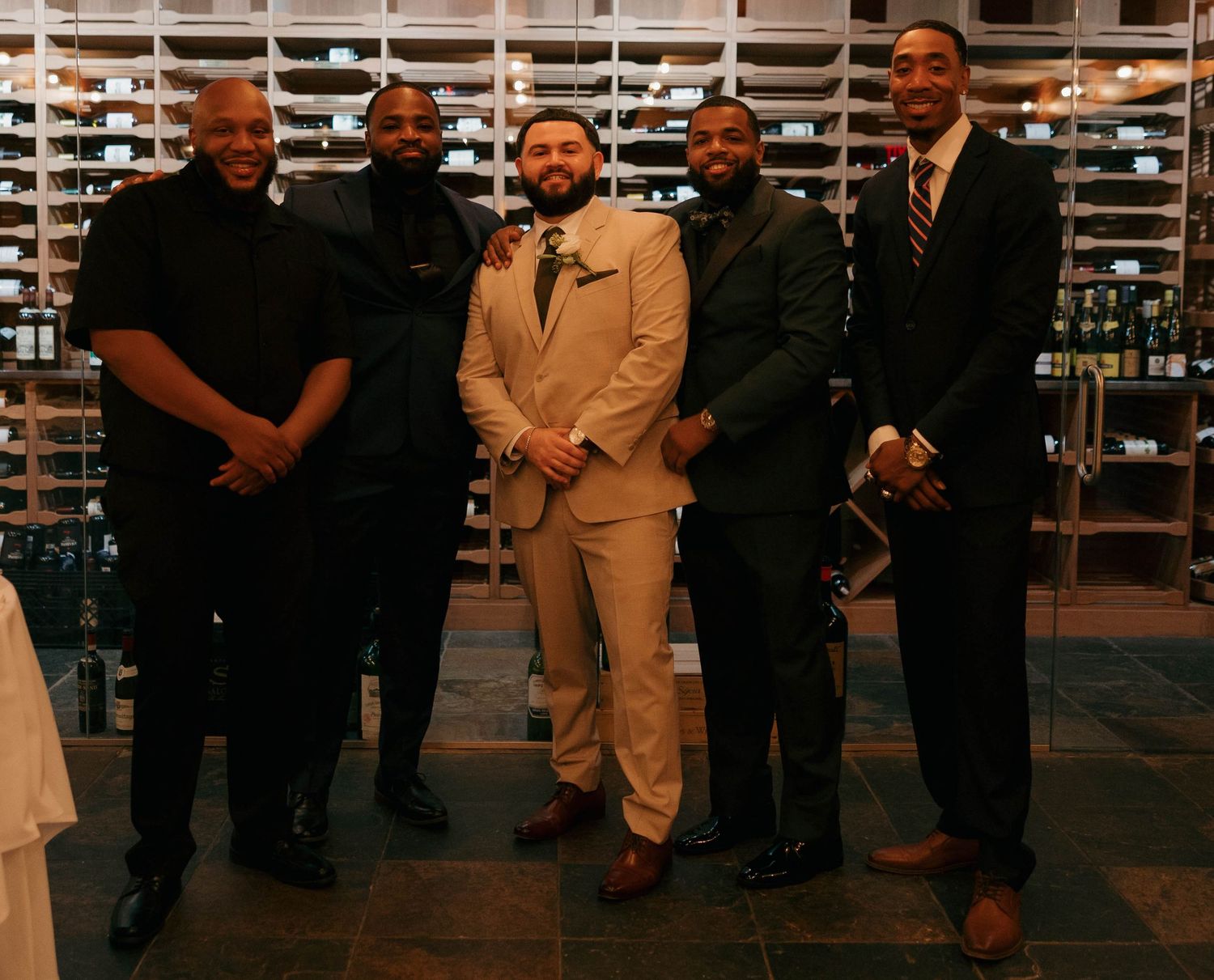 Wedding party members pose formally in front of extensive wine storage.