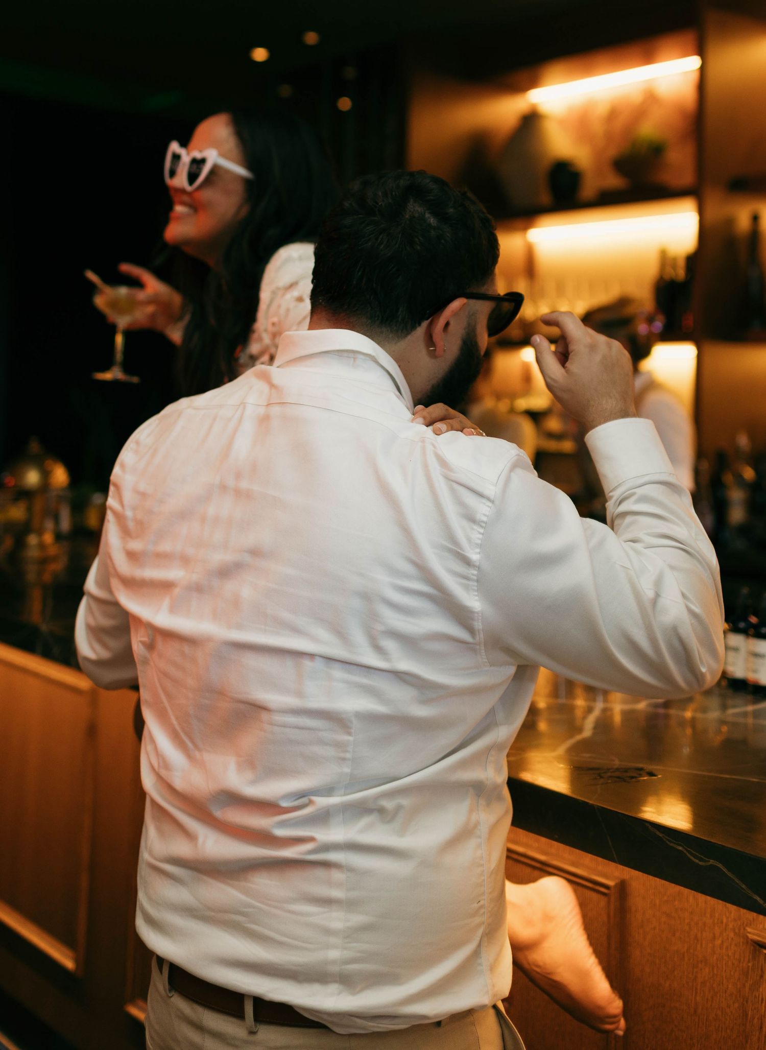 Person in white shirt sitting at an illuminated bar counter with warm ambient lighting.