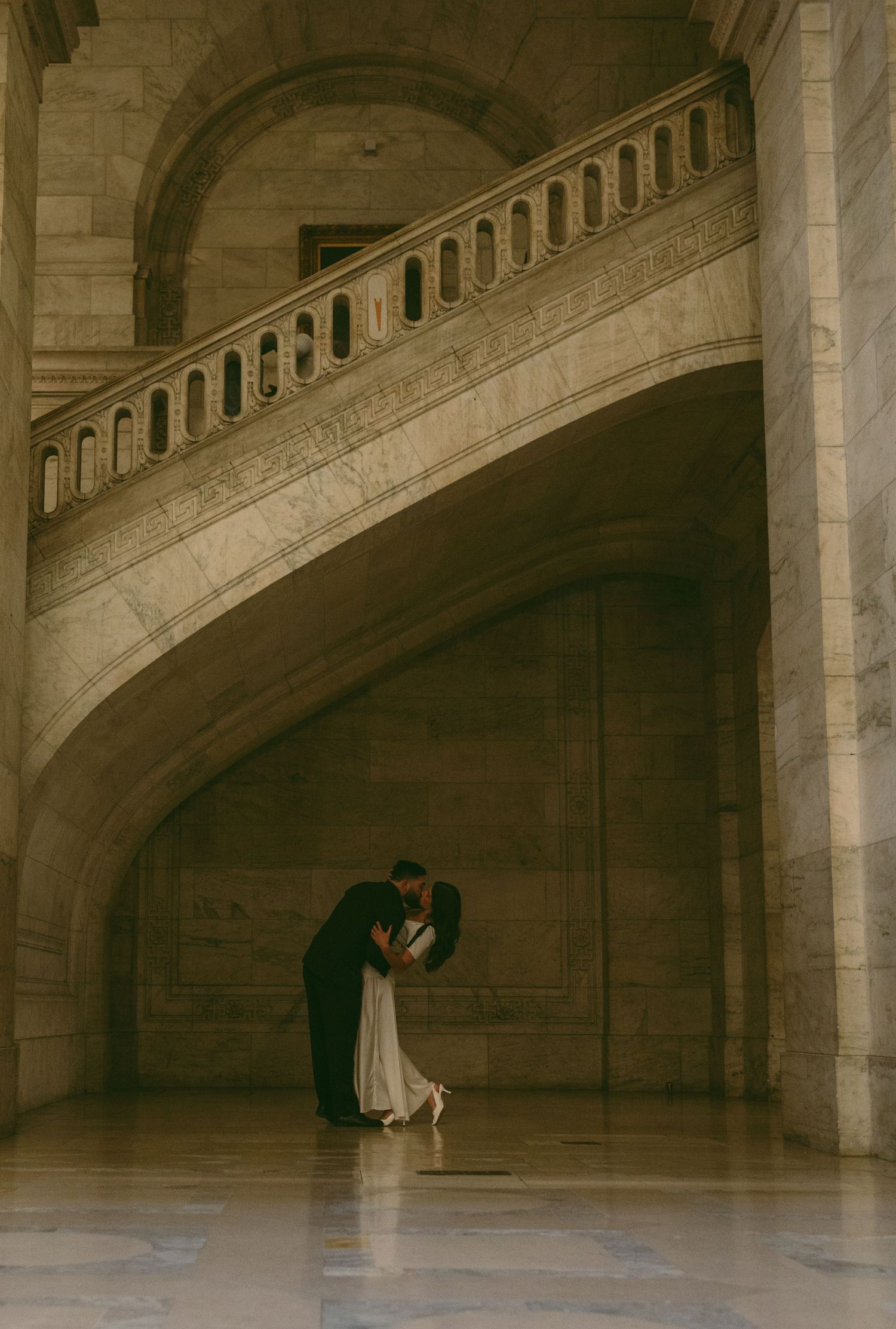 A romantic dance moment captured under a sweeping marble staircase in warm vintage tones.