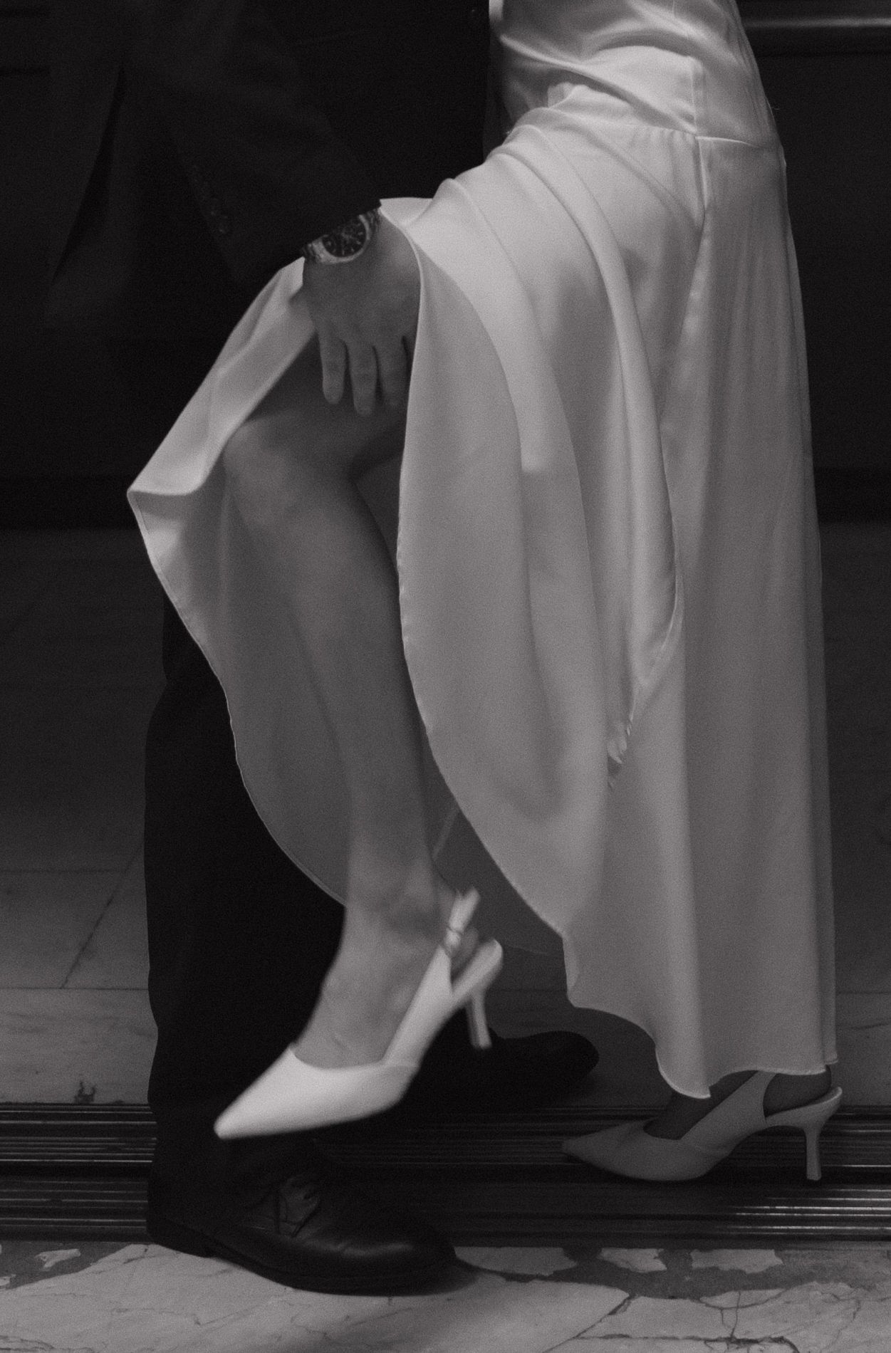Close-up of formal shoes and white dress hem on a marble floor.